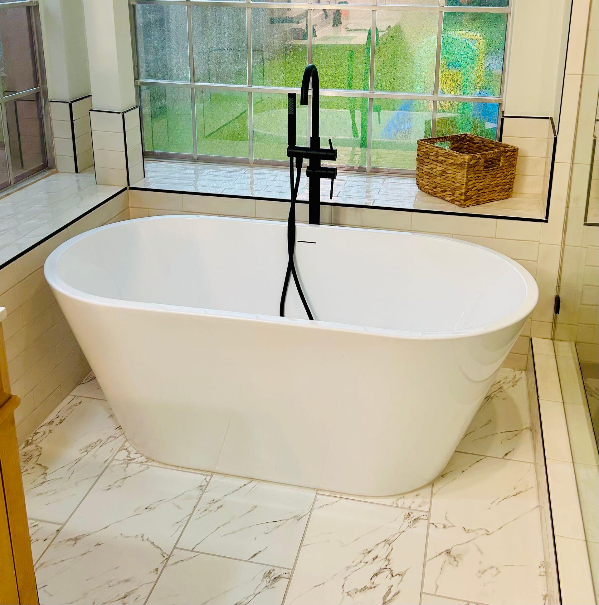 White freestanding bathtub in a bathroom with window, black faucet, and woven basket.