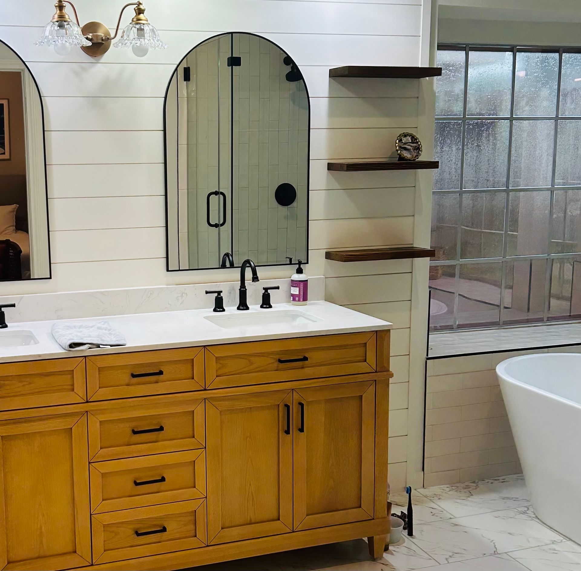 Bathroom with a yellow vanity, arched mirrors, and a white bathtub.