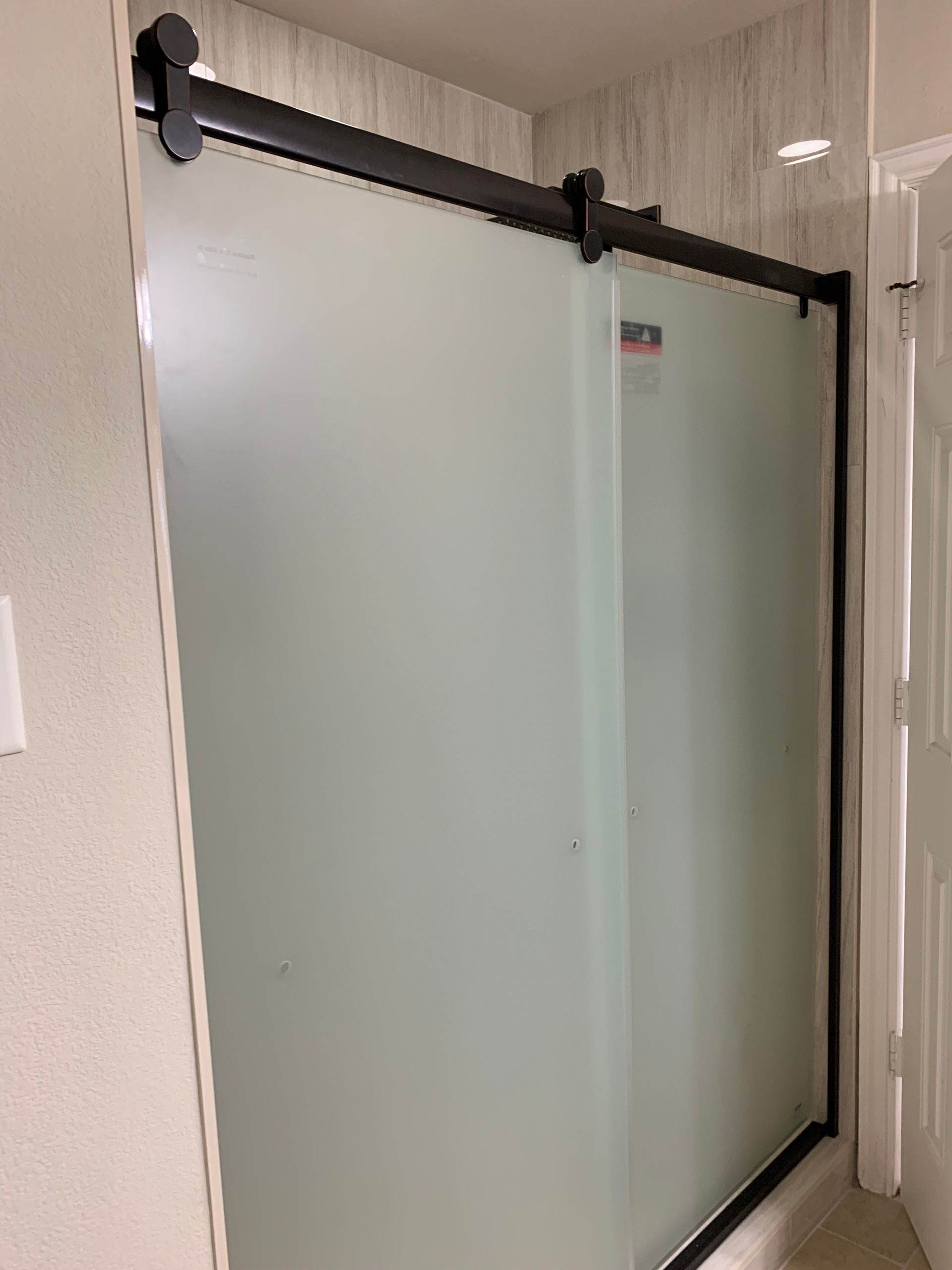 Frosted glass shower door with black hardware in a bathroom.