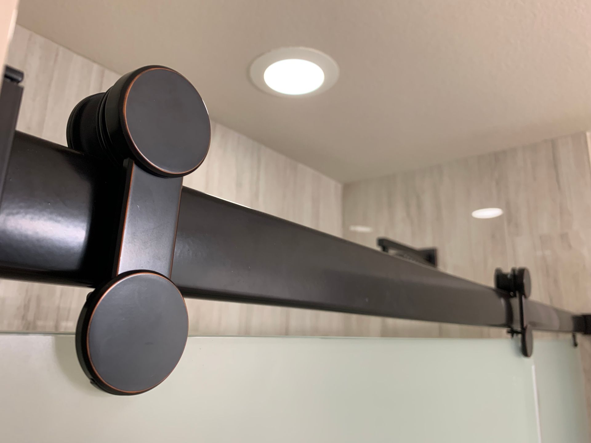 Dark bronze sliding door track and rollers installed on a bathroom wall.