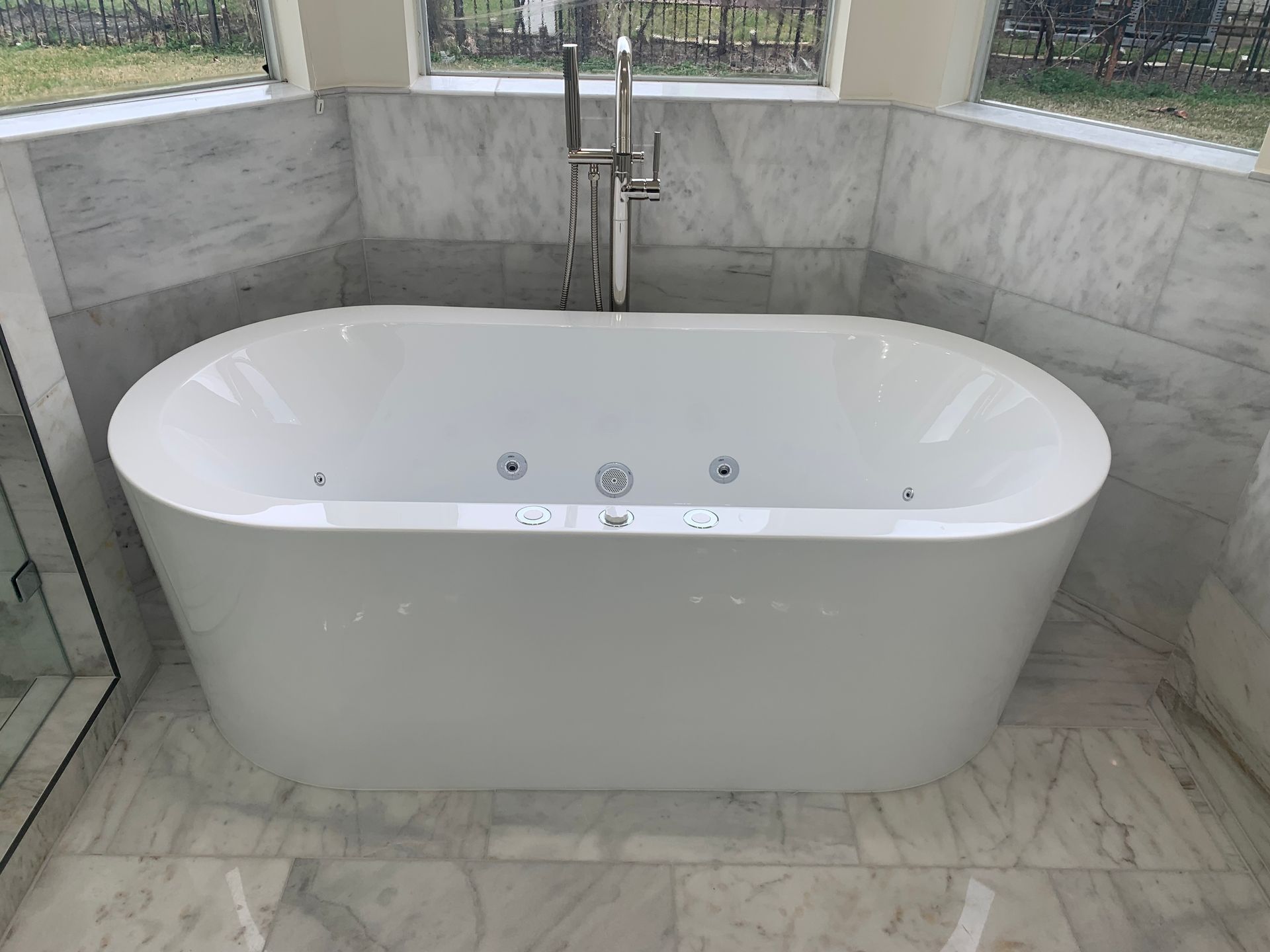 White oval freestanding bathtub in a marble-tiled bathroom. 