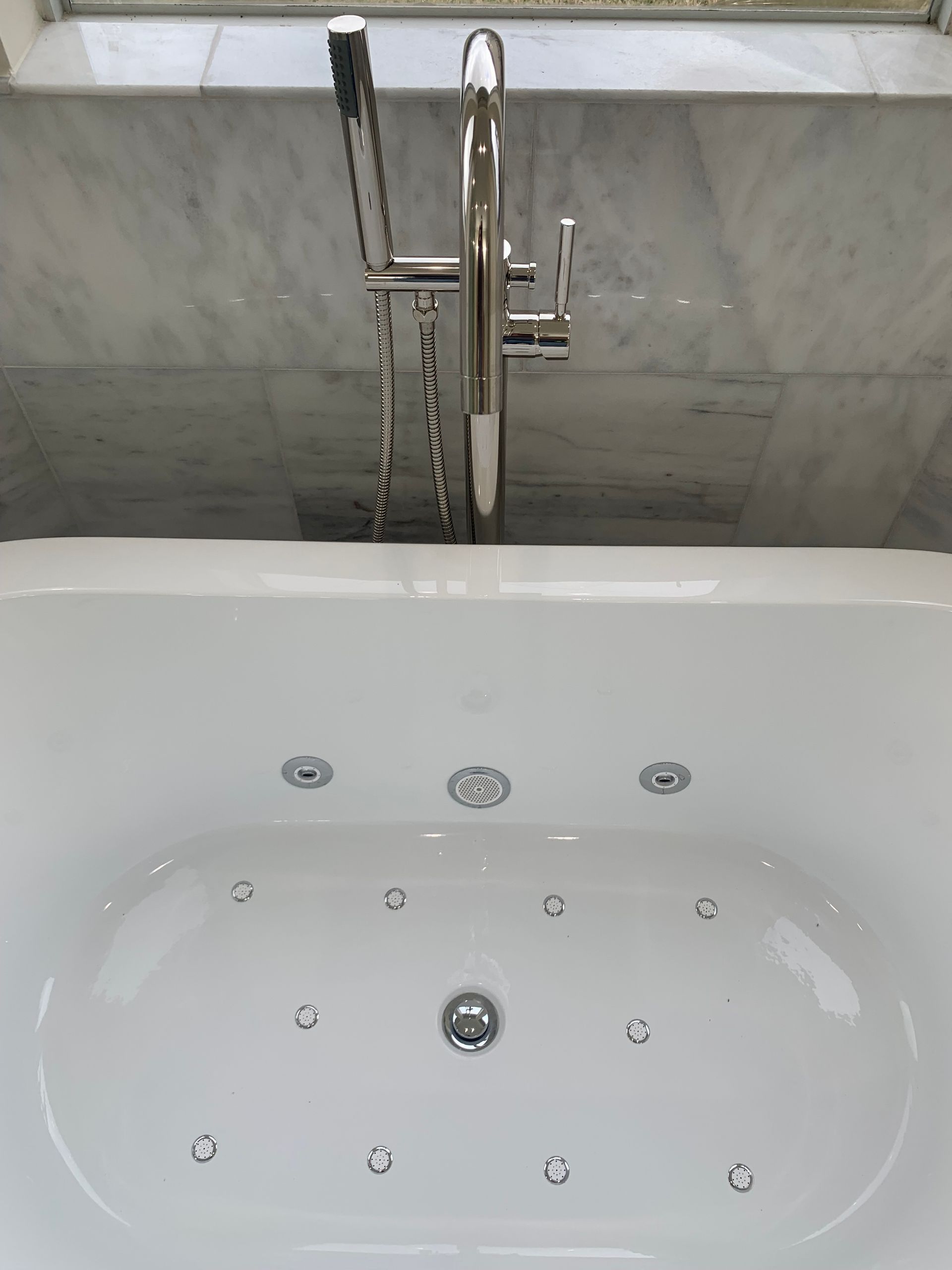 White bathtub with chrome faucet, water flowing. Marble backsplash.