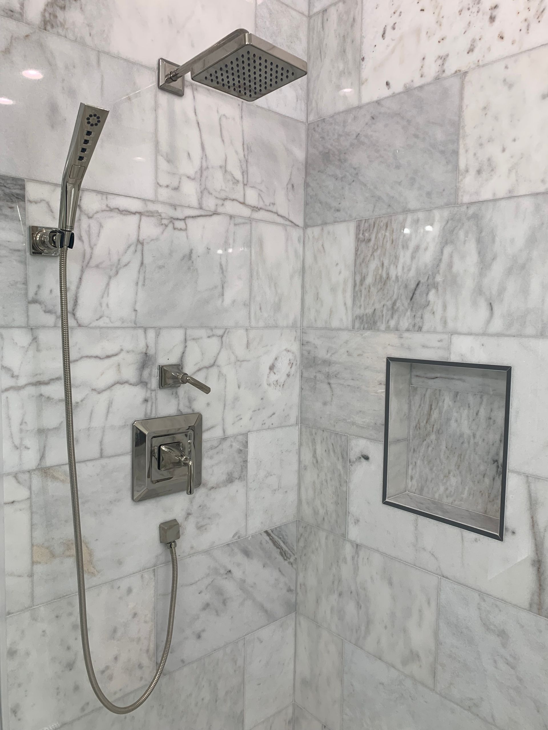 Shower with white marble tile and silver shower fixtures.