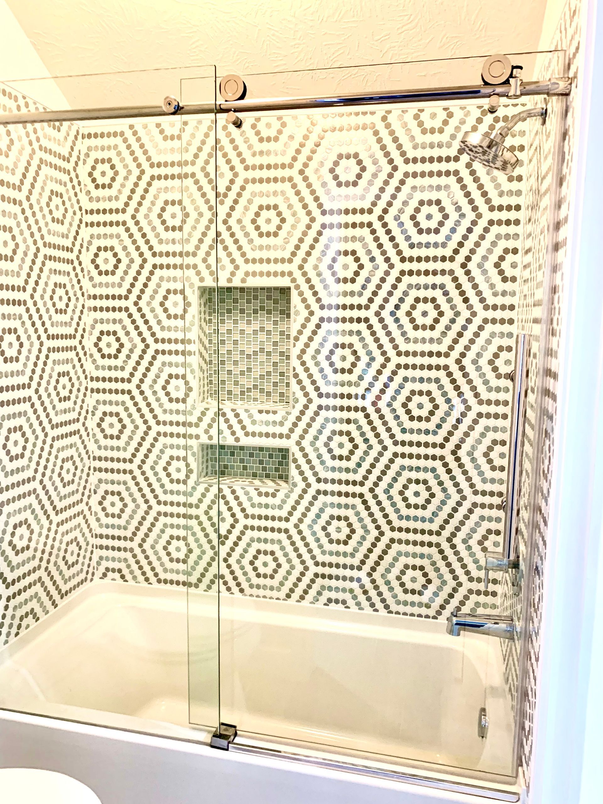 Bathroom with hexagonal patterned tile, glass shower doors, and a bathtub.