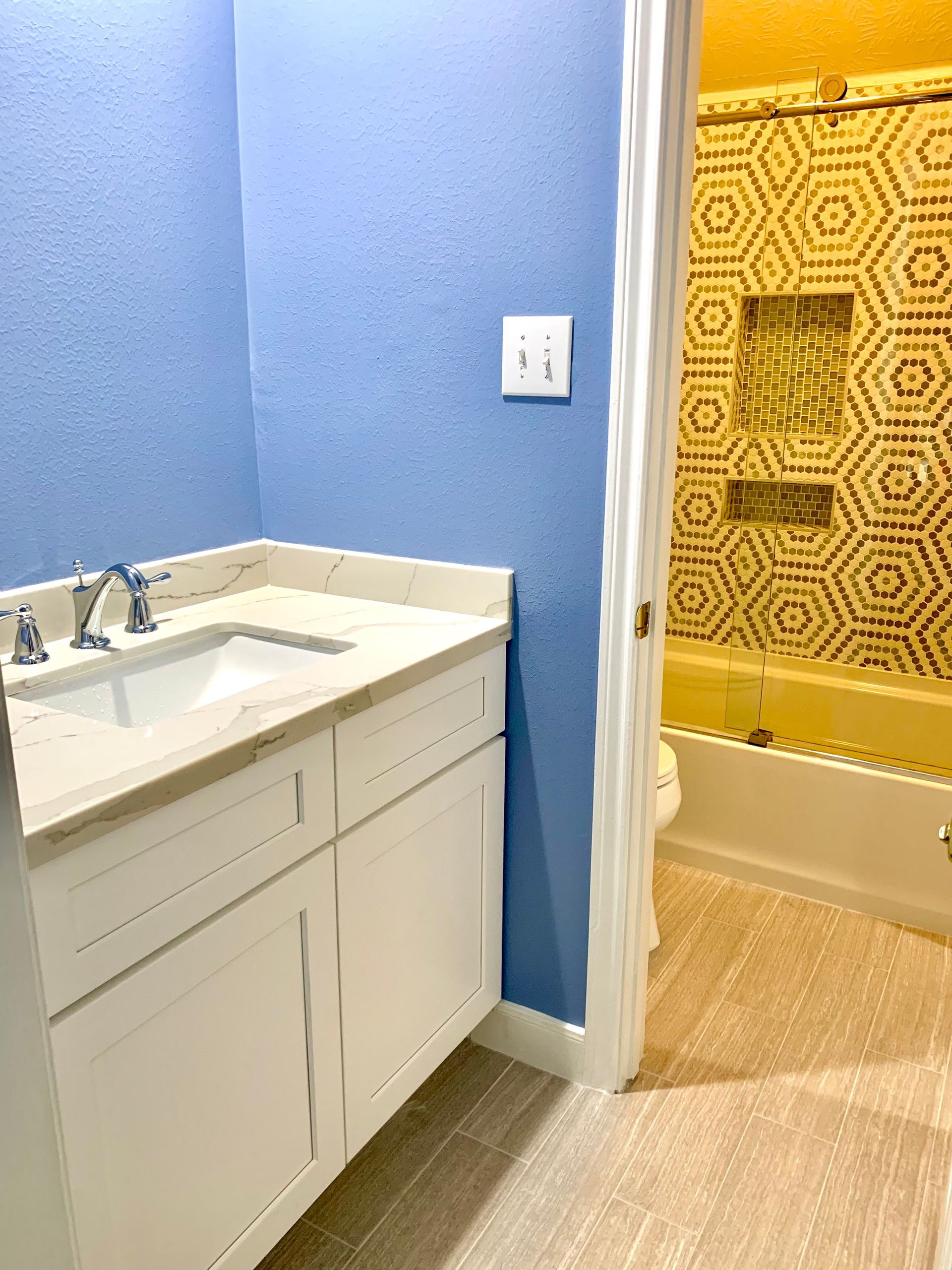 Bathroom with blue walls, white vanity, and gold-tiled shower/tub area.