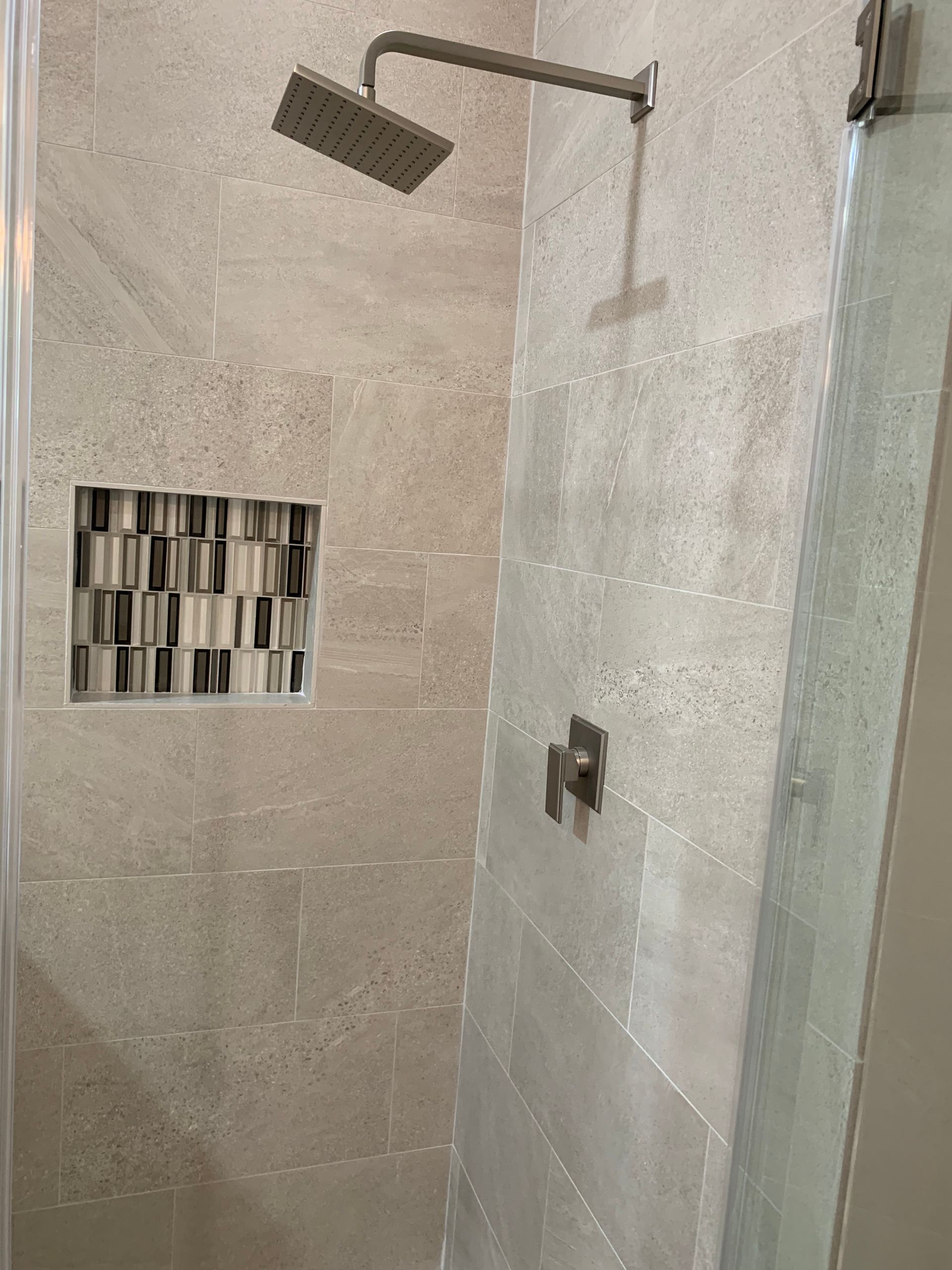 Shower with gray tiled walls, recessed shelf with mosaic tiles, and a square shower head.