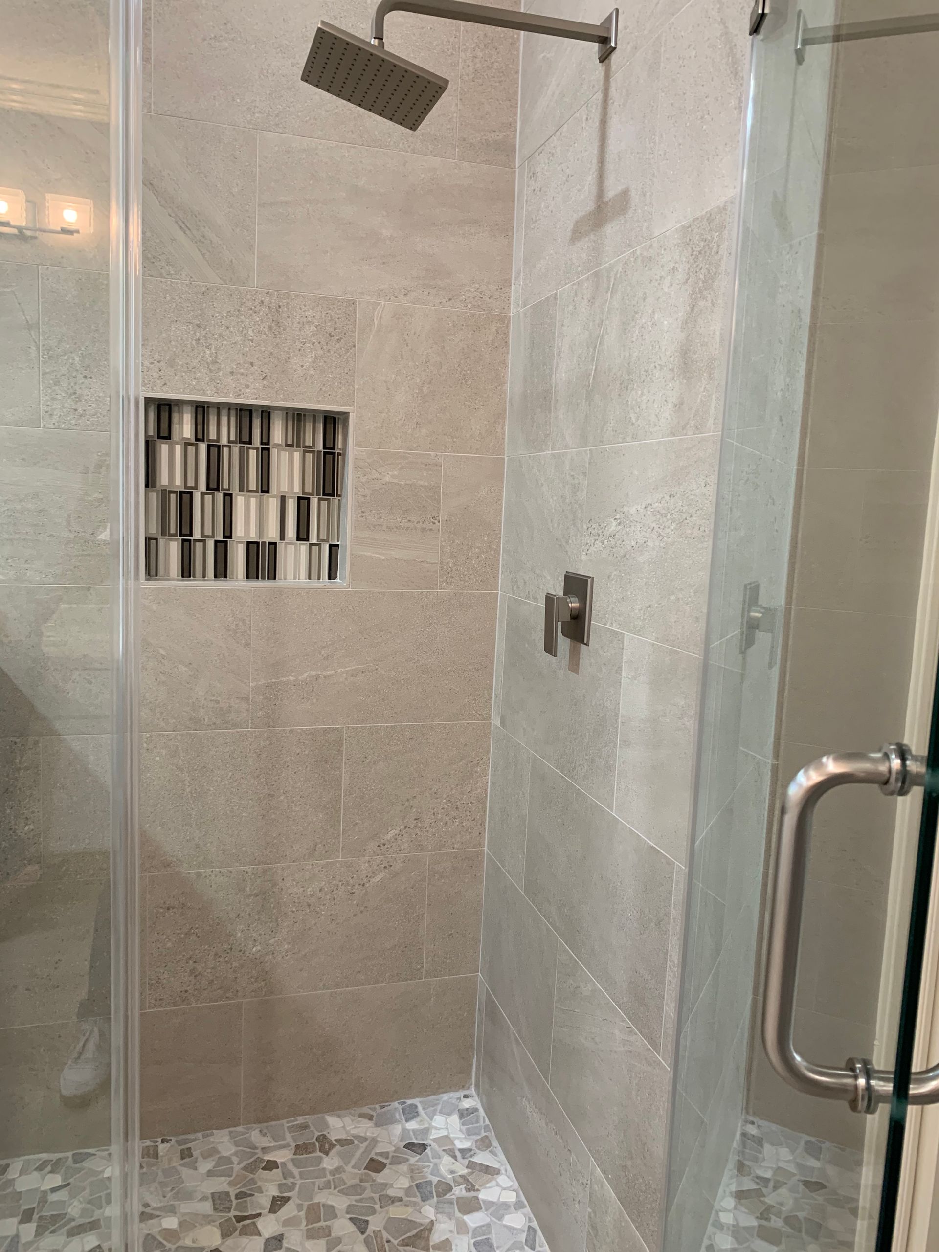 Shower with gray tiled walls, glass door, and patterned niche.