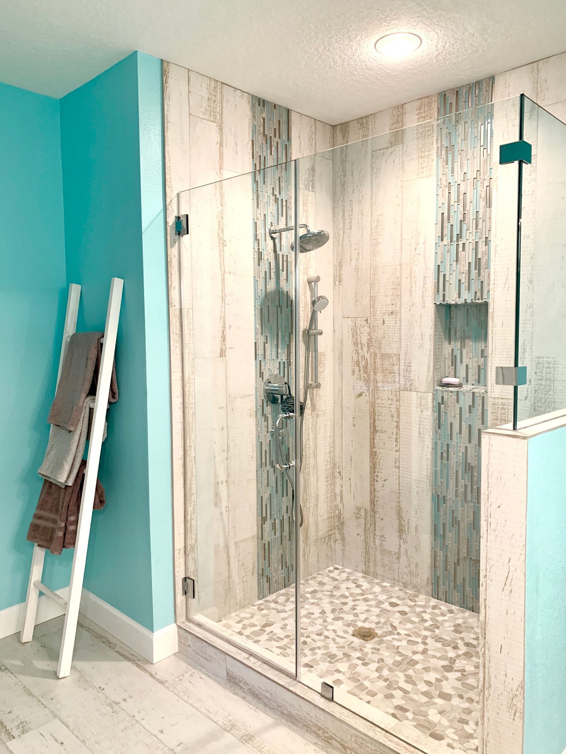 Blue and white bathroom with a glass shower and pebble floor.