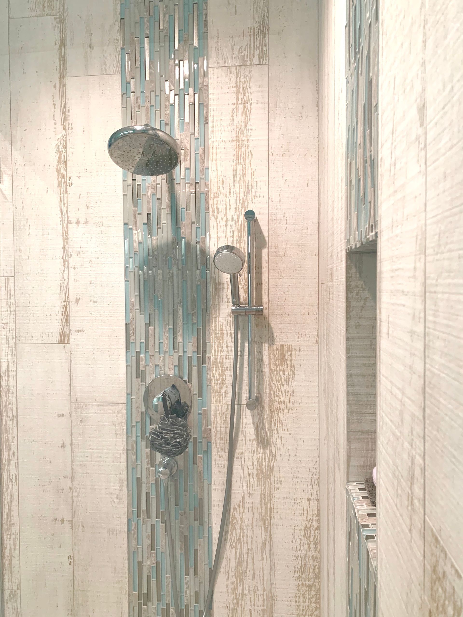 Shower stall with blue and white tile, shower head and handheld sprayer.