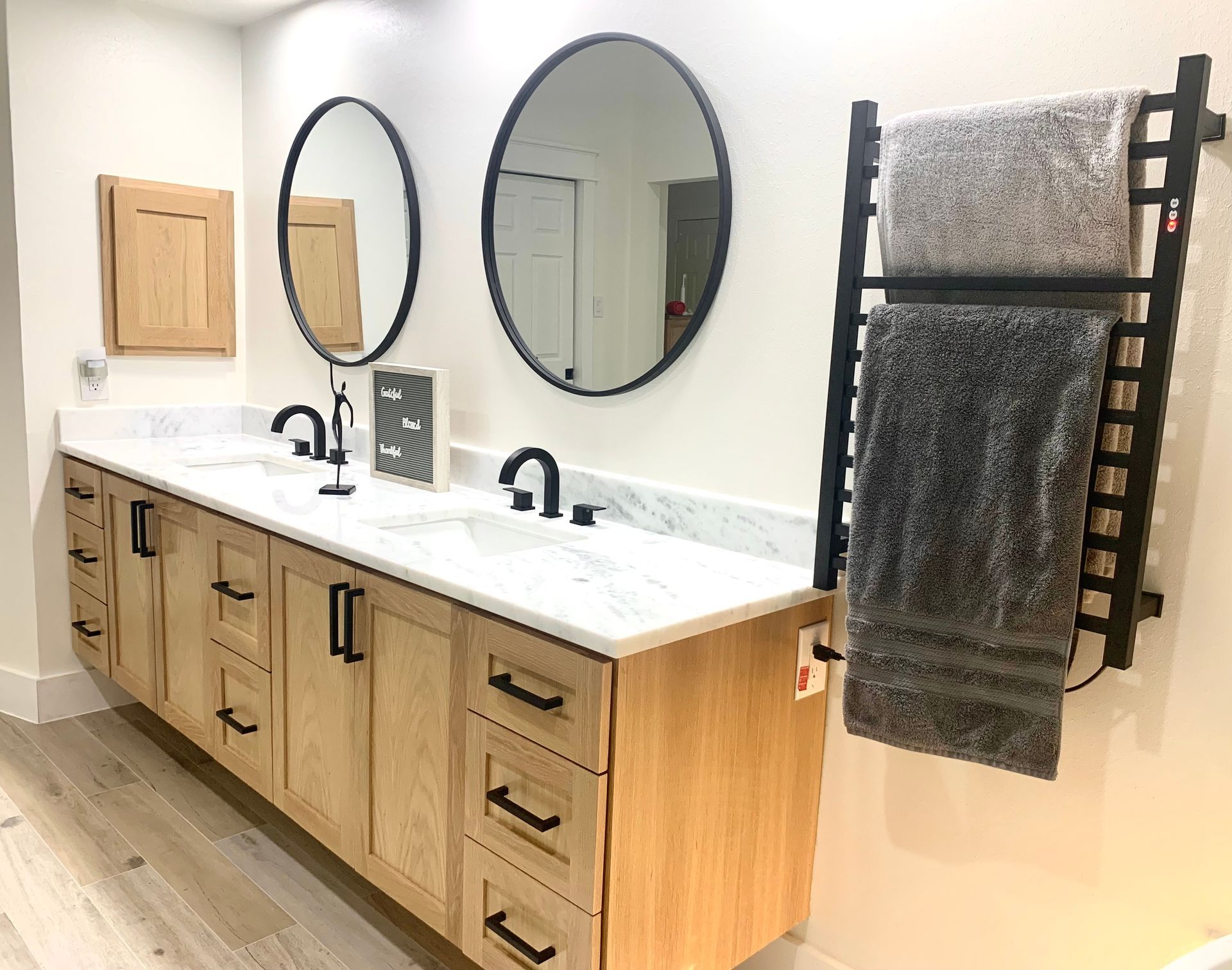 Bathroom with double sink vanity, two round mirrors, and heated towel rack.