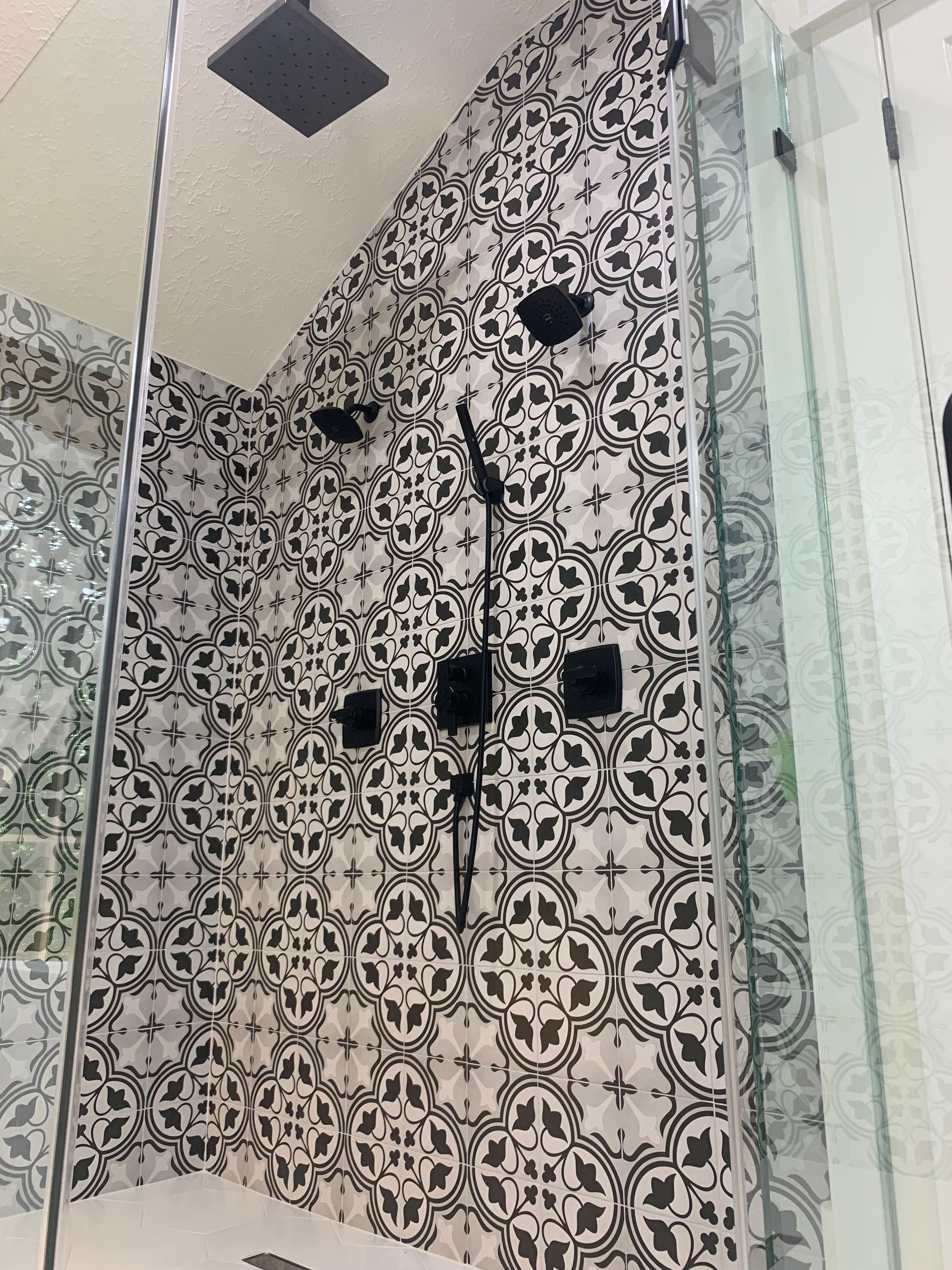 Shower with black fixtures and patterned tile, glass enclosure.