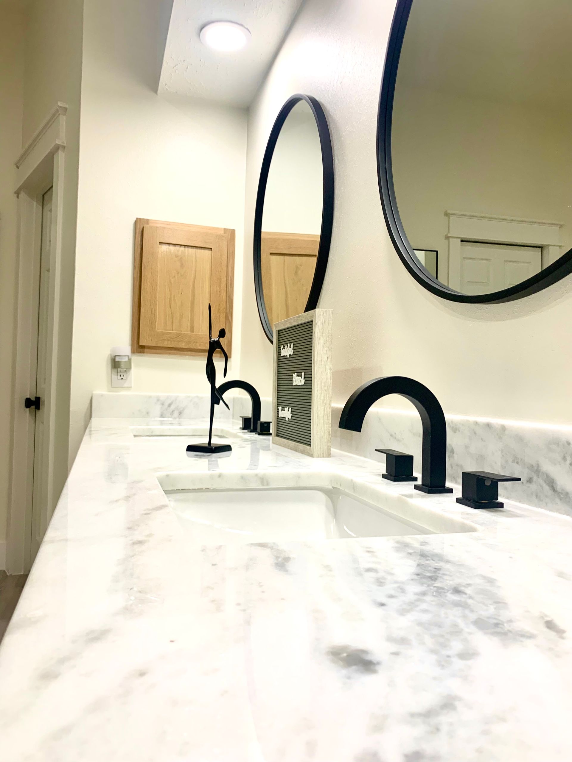 Bathroom vanity with two sinks, black faucets, and round mirrors above a white marble countertop.