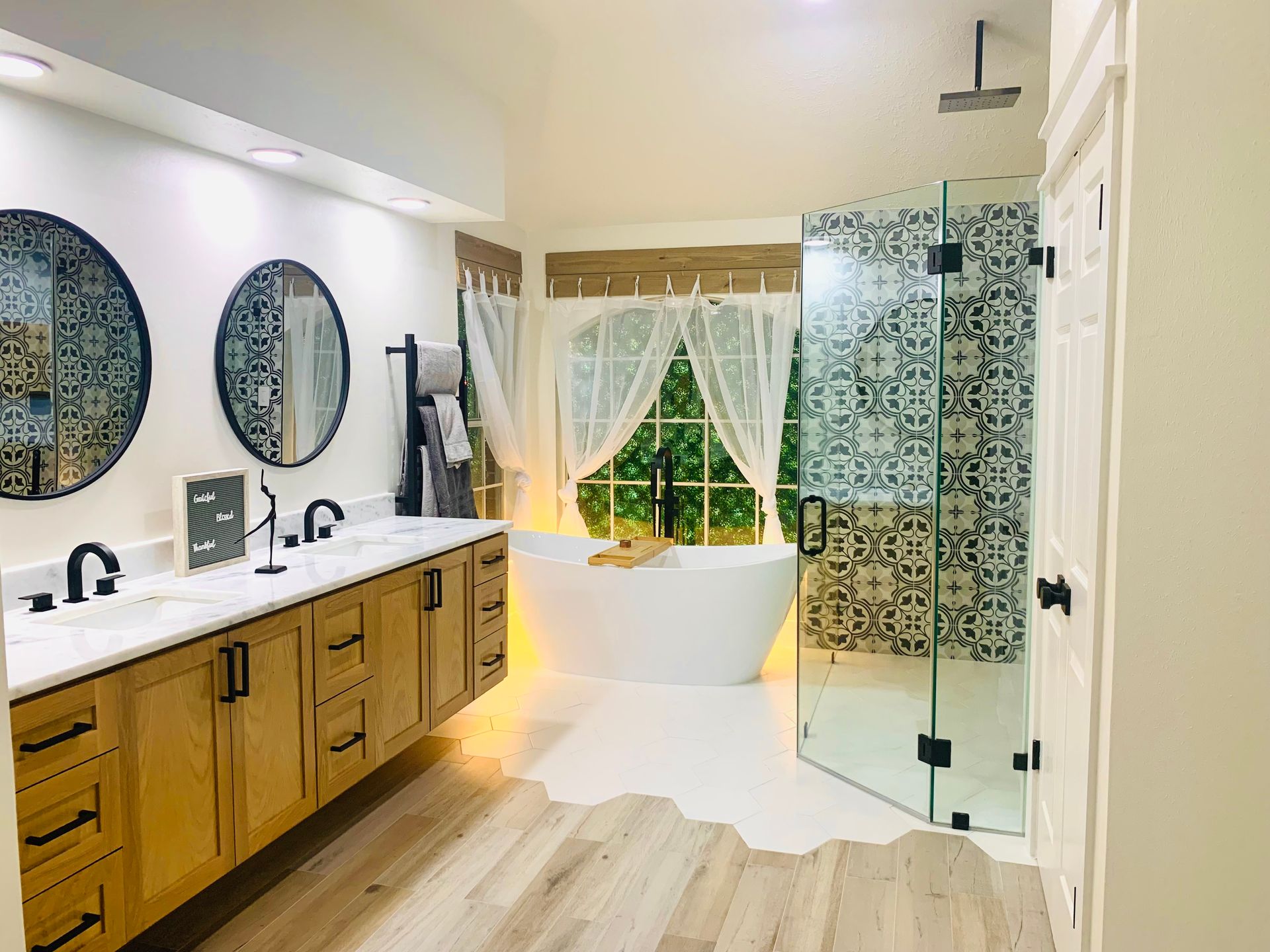 Bathroom with a large vanity, freestanding tub, patterned shower, and a large window.
