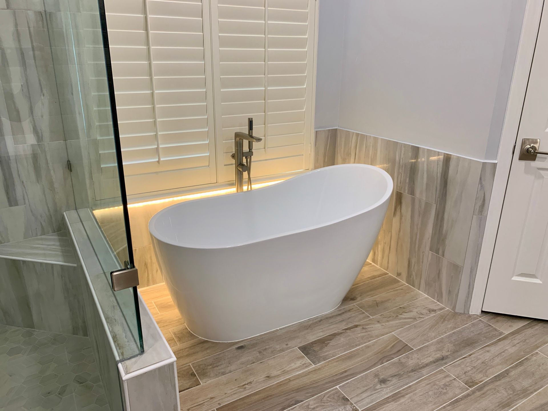 Modern bathroom with white freestanding tub, wood-look tile, and gold faucet.