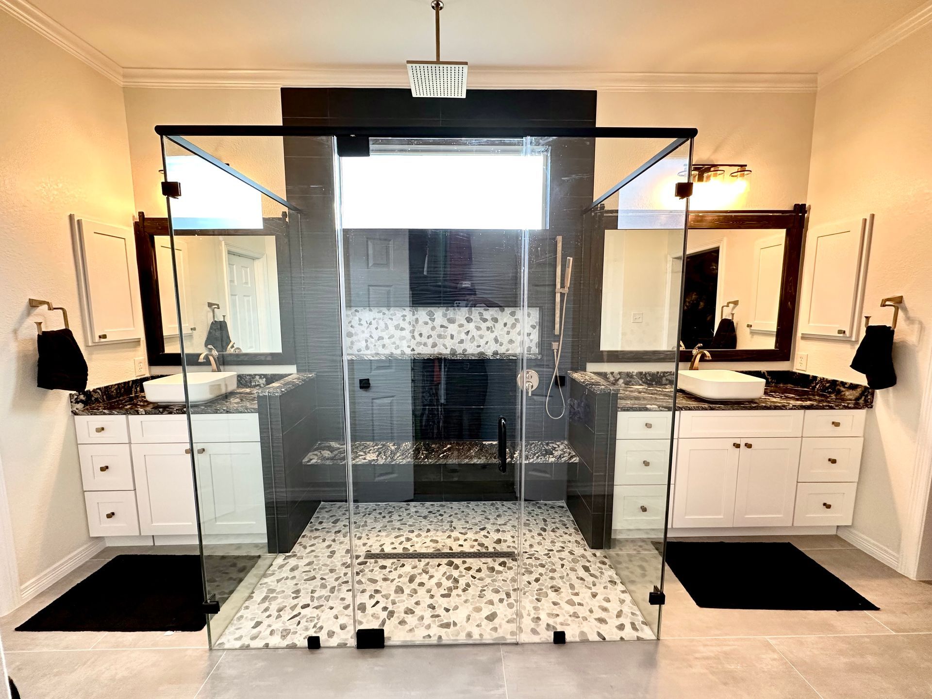 Spacious bathroom with glass shower, two vanities, and stone flooring.