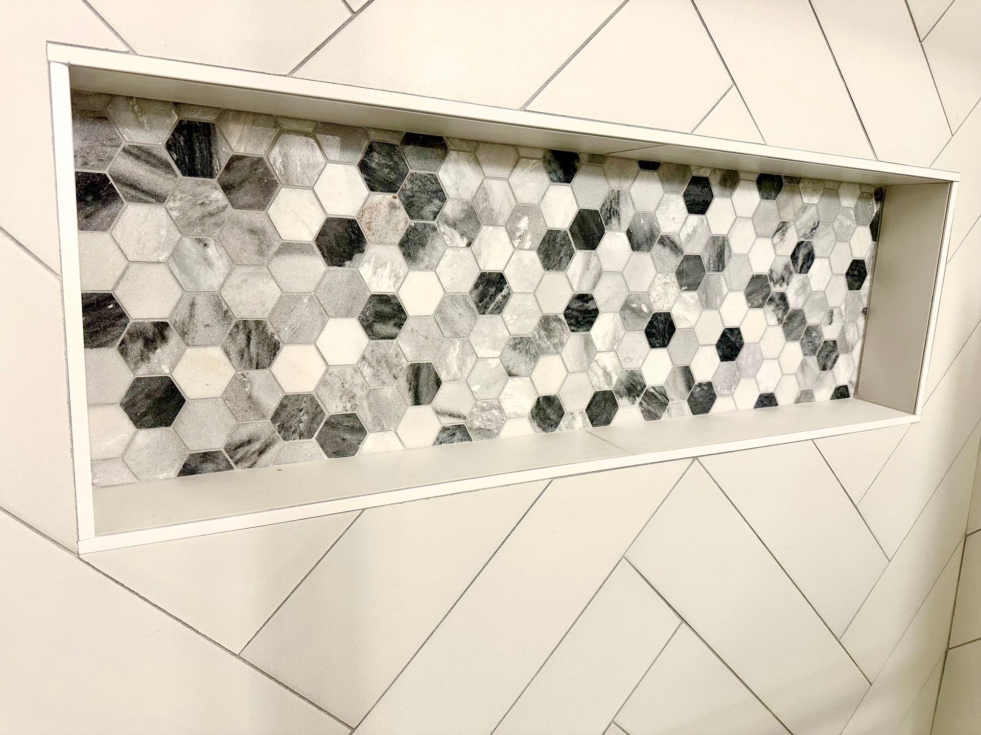 Recessed shower shelf with hexagon tile, framed by white tiles in a herringbone pattern.