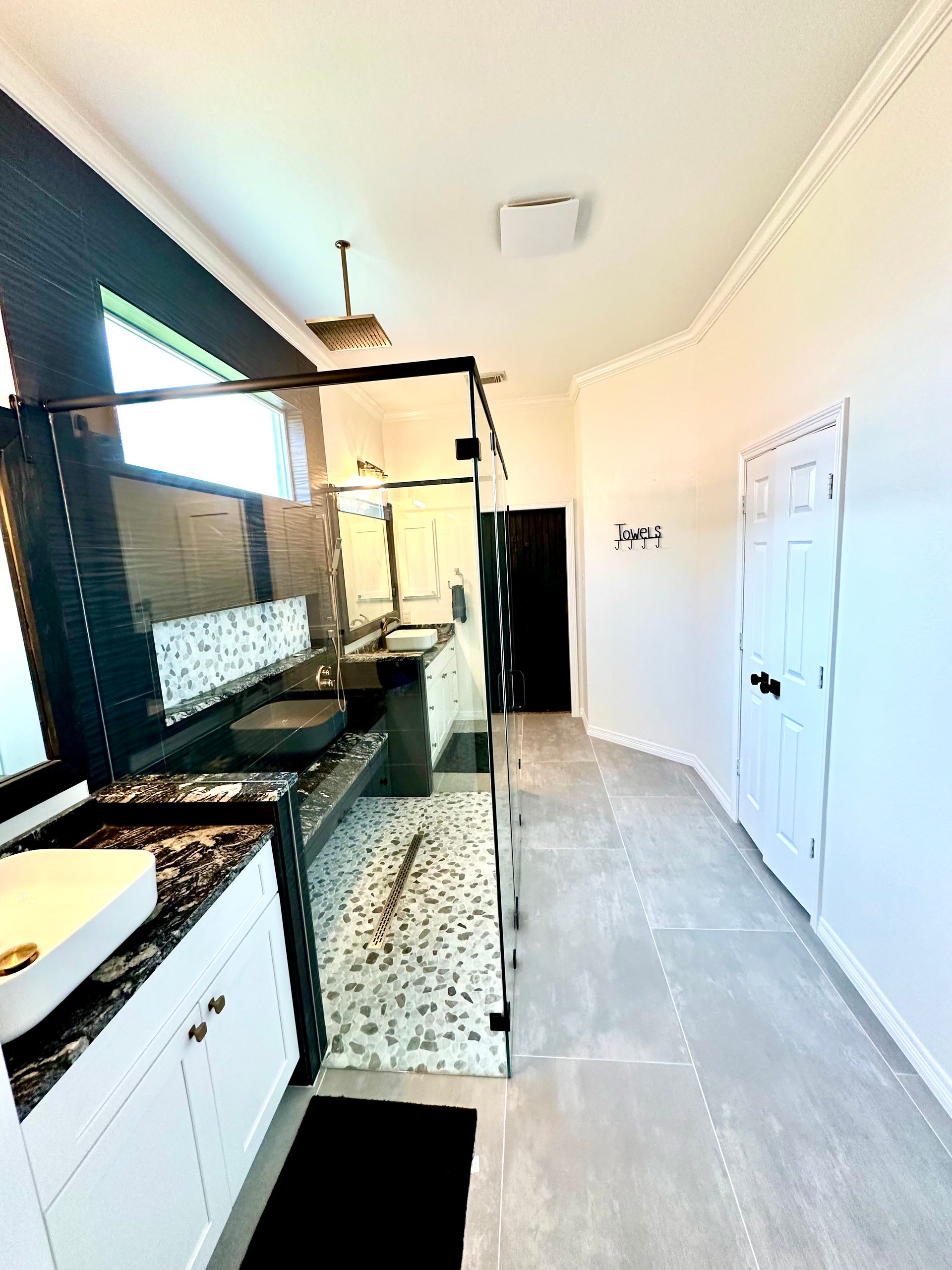 Modern bathroom with white cabinets, dark countertops, a glass shower, and a white door.