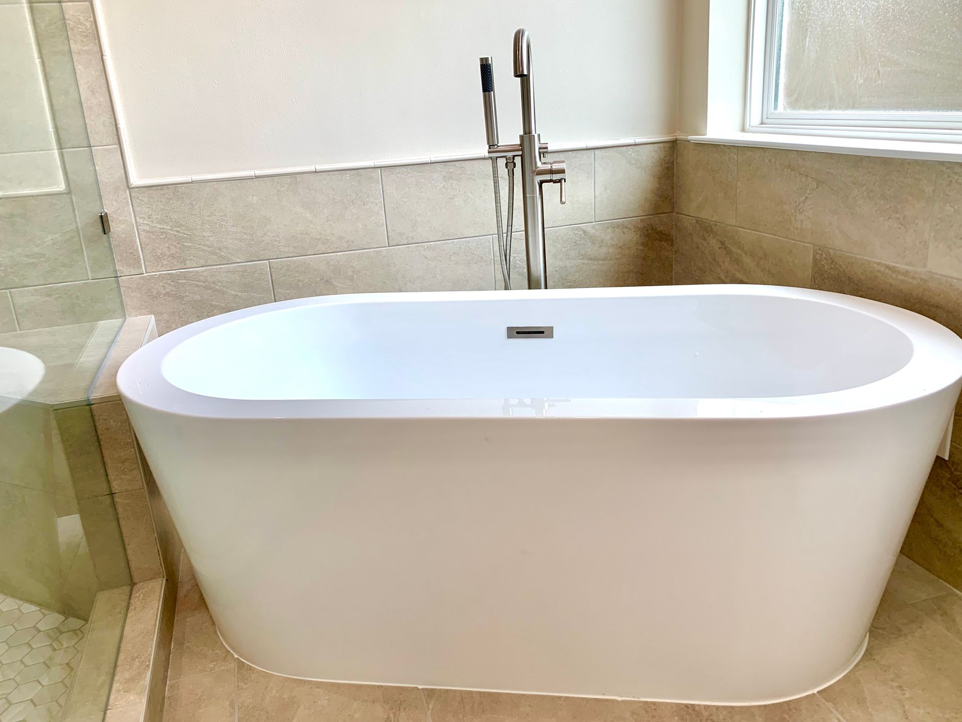 White oval bathtub with tall chrome faucet in a tiled bathroom.