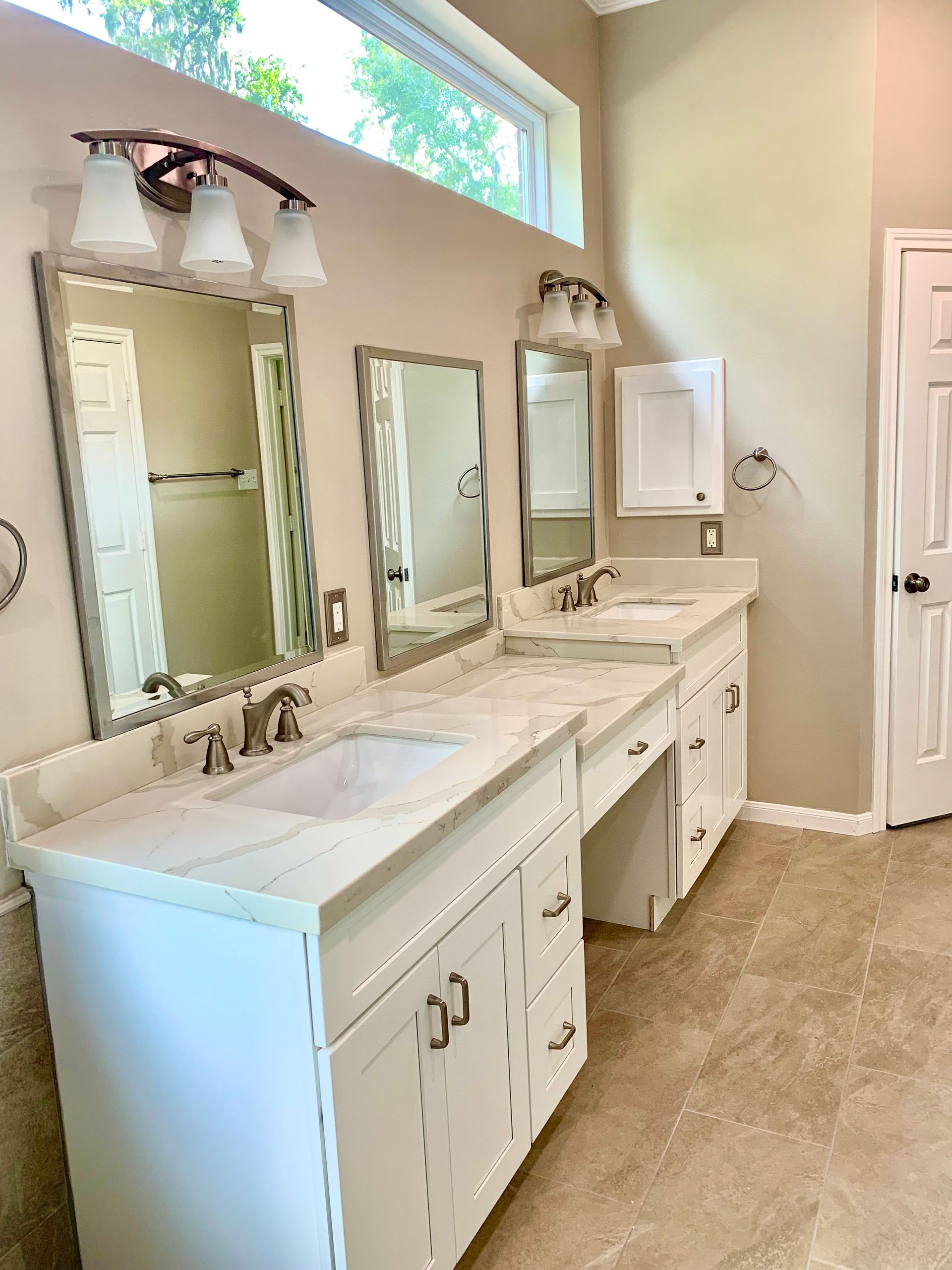 A bright bathroom with a double vanity and mirrors, cream walls, and tile flooring.