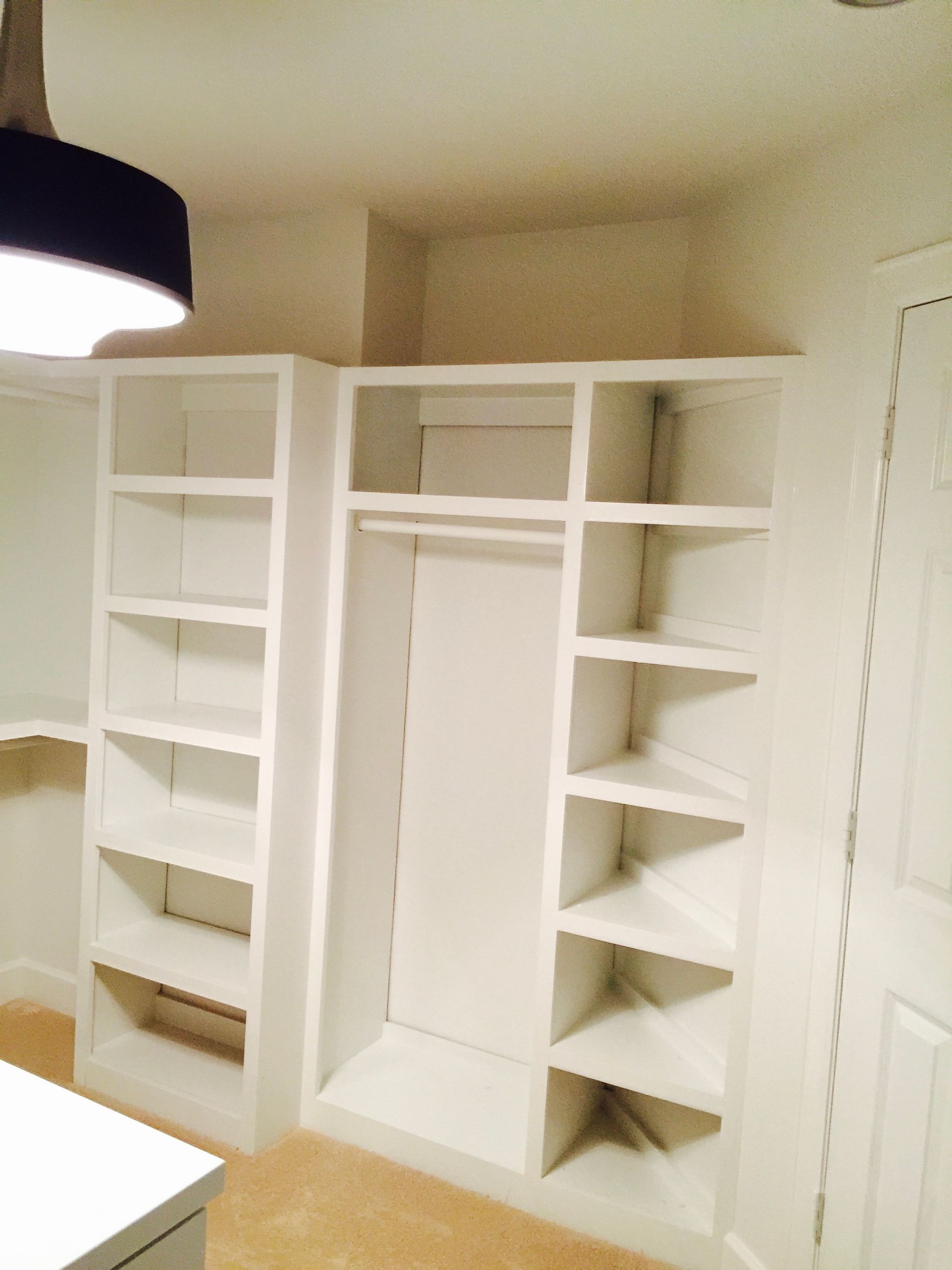 Built-in white closet shelving with a hanging rod and shelves on either side, in a room.