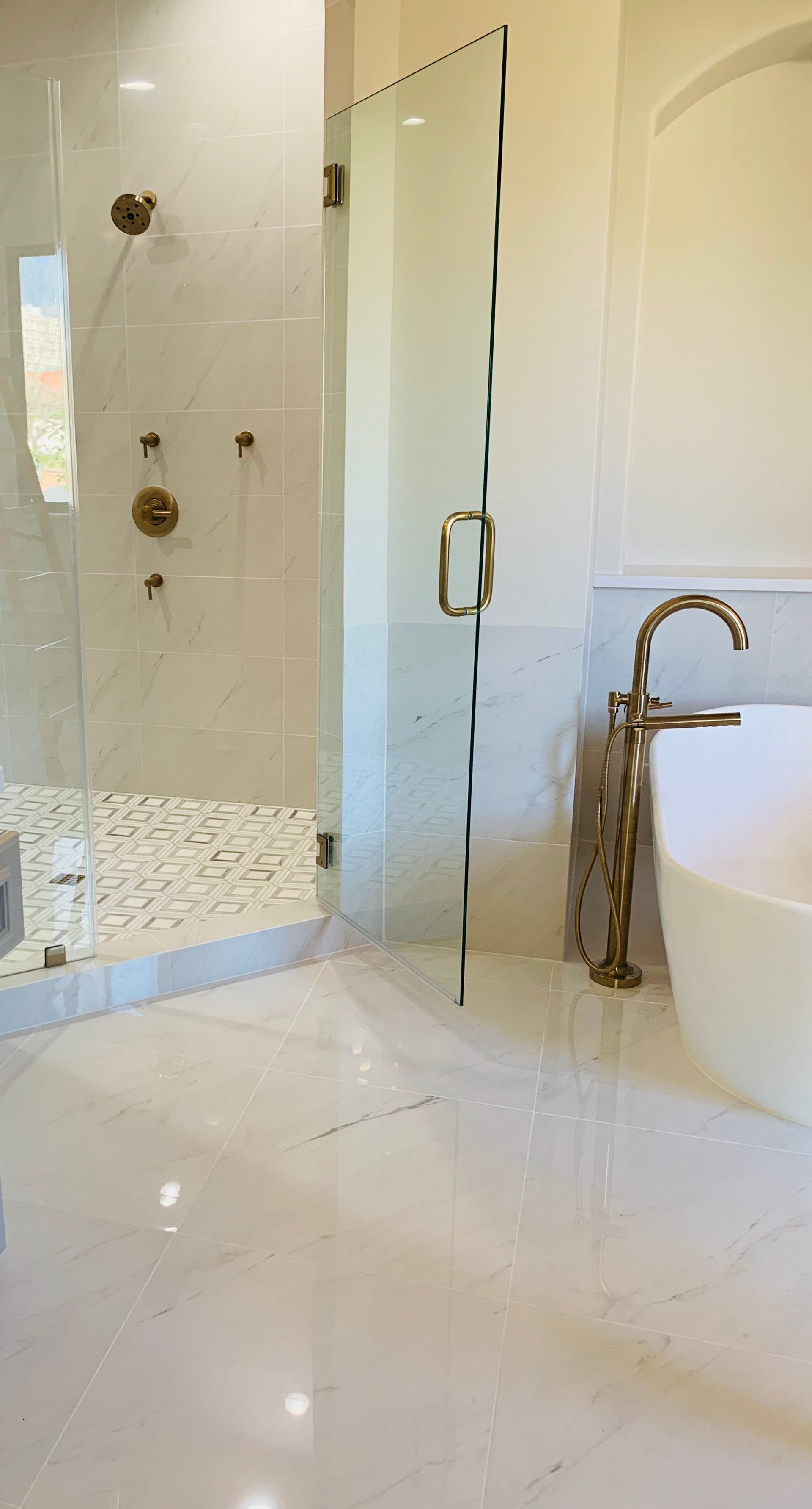 Bathroom with glass shower, white flooring, gold fixtures, and a freestanding tub.