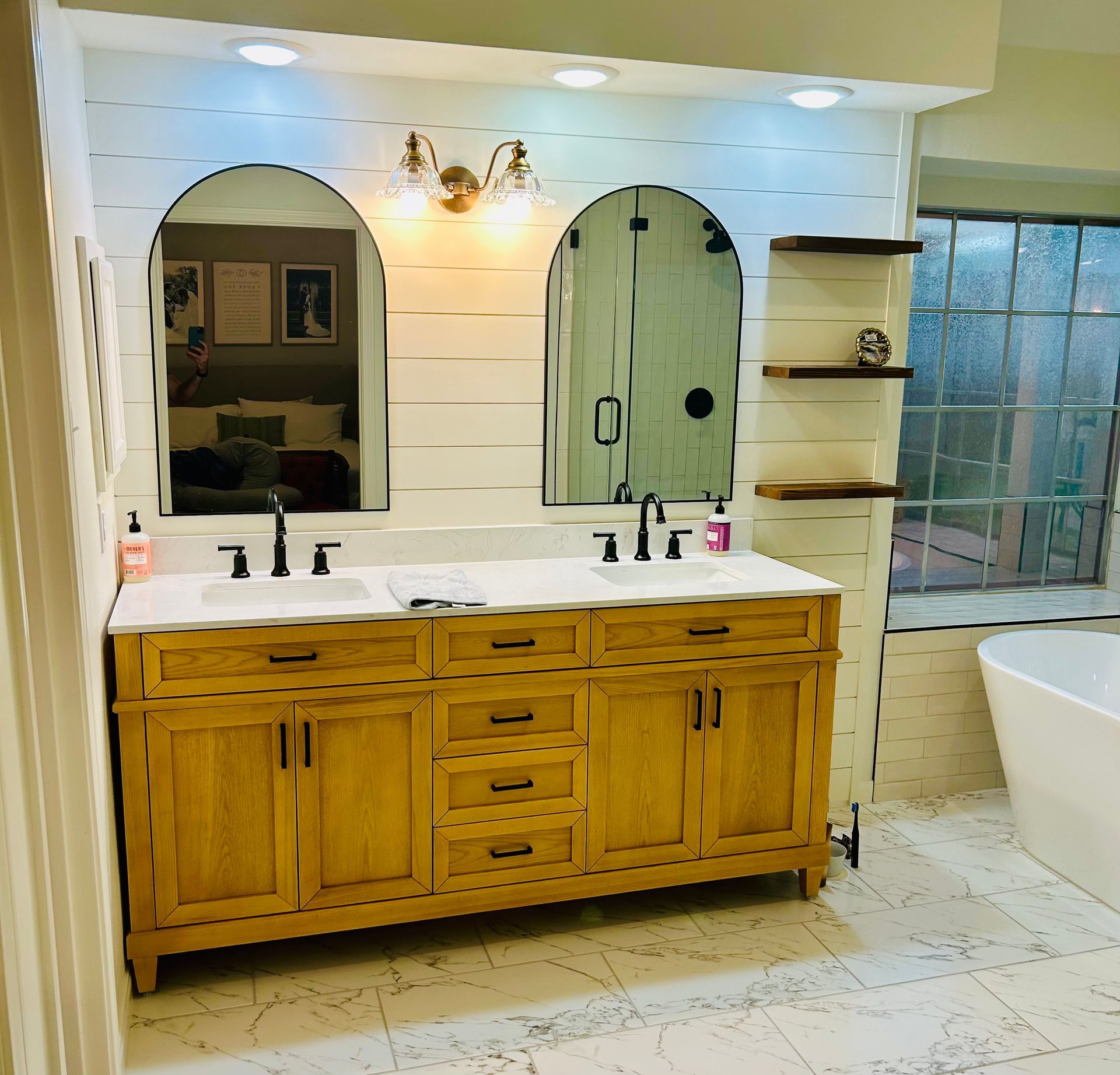 Bathroom with wood vanity, arched mirrors, and a white soaking tub.