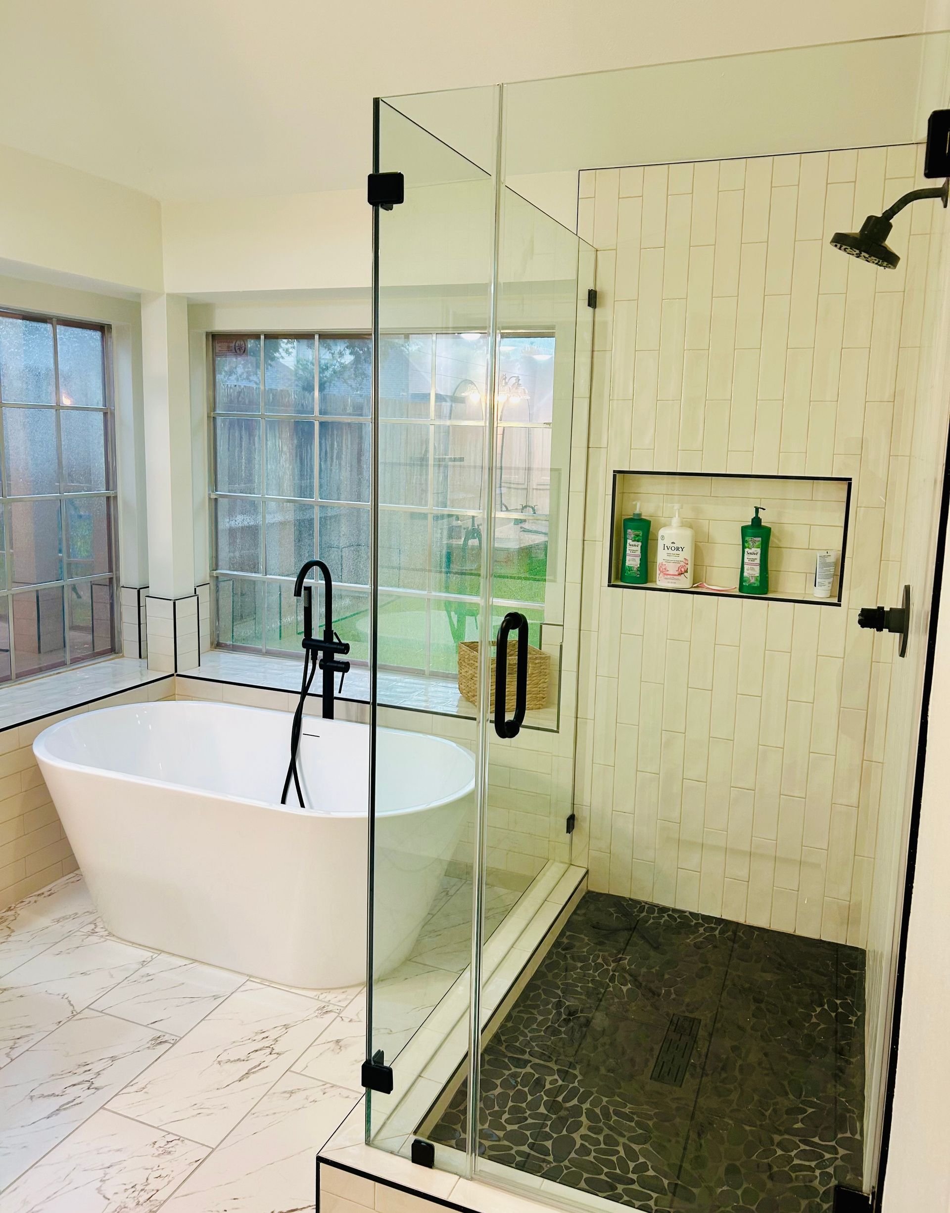 Modern bathroom with a glass-enclosed shower, freestanding tub, and light-colored tile.