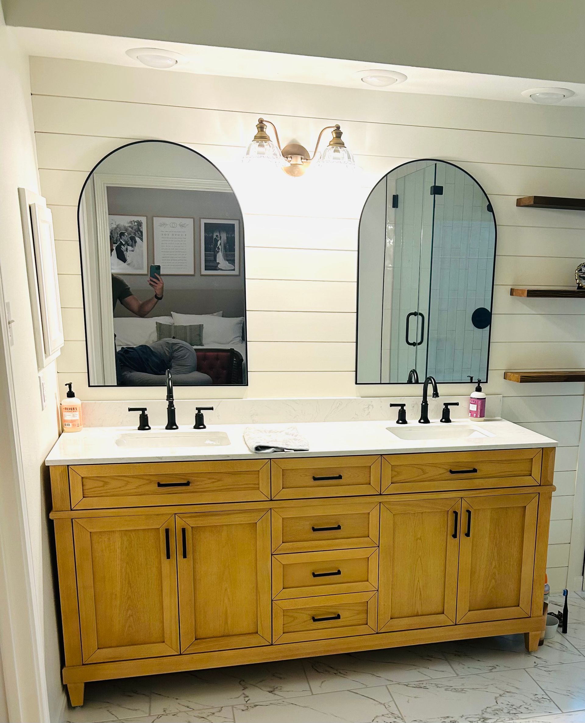 Bathroom with arched mirrors, wood vanity, and shiplap walls. 