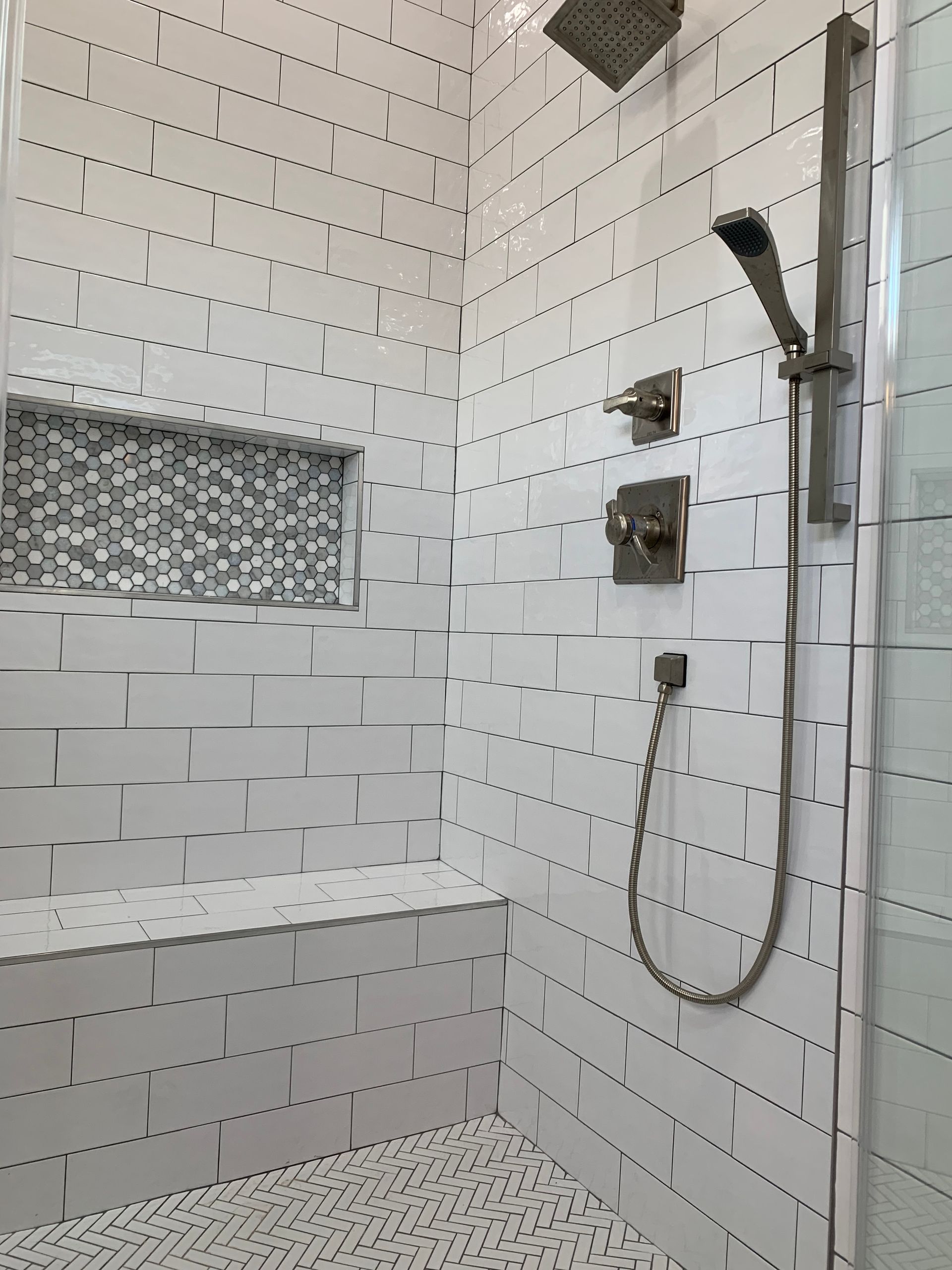 White tiled shower with built-in bench, shower head, and handheld shower.