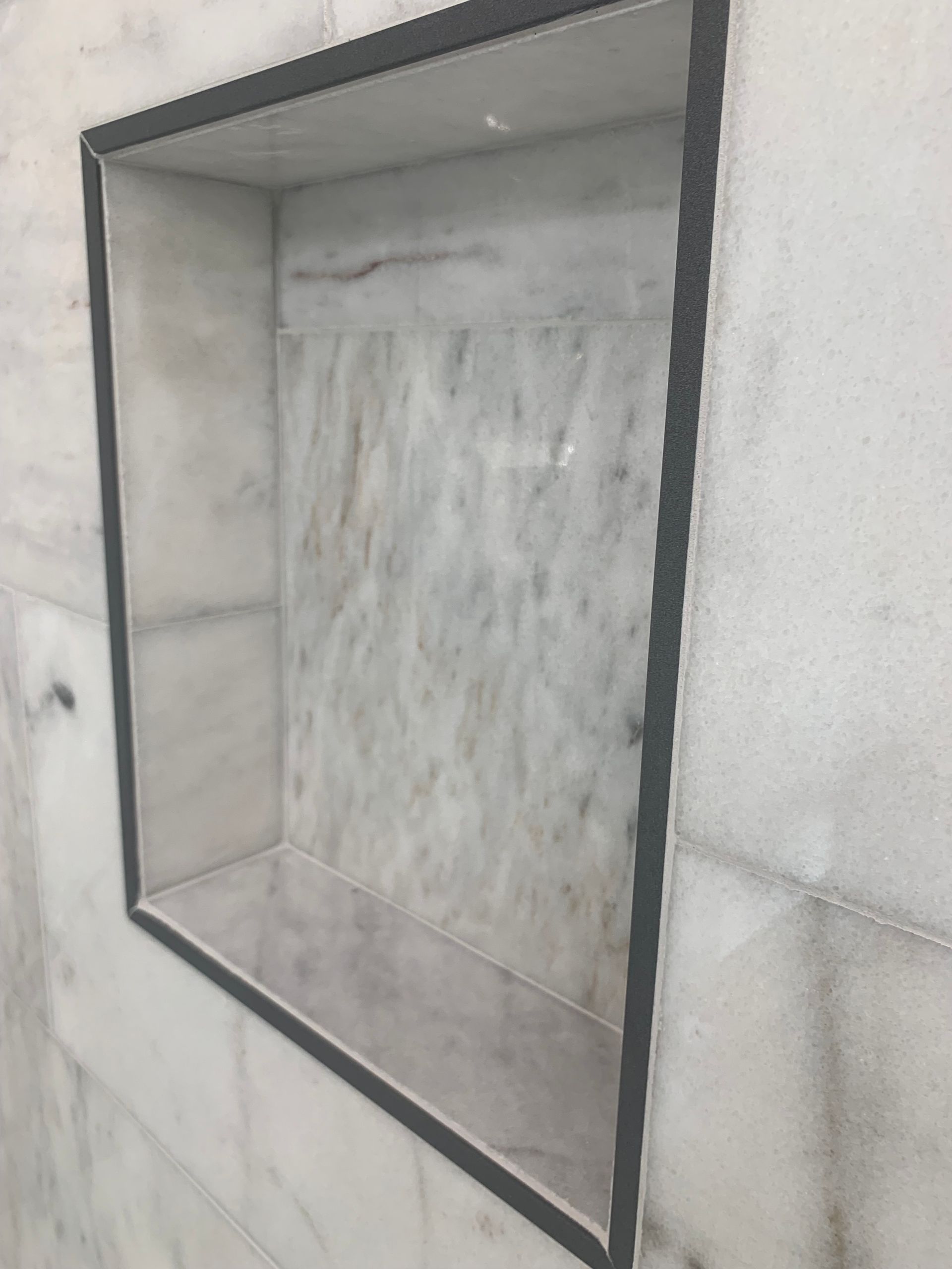 Recessed marble shower shelf, outlined in black, set into marble tiled wall.