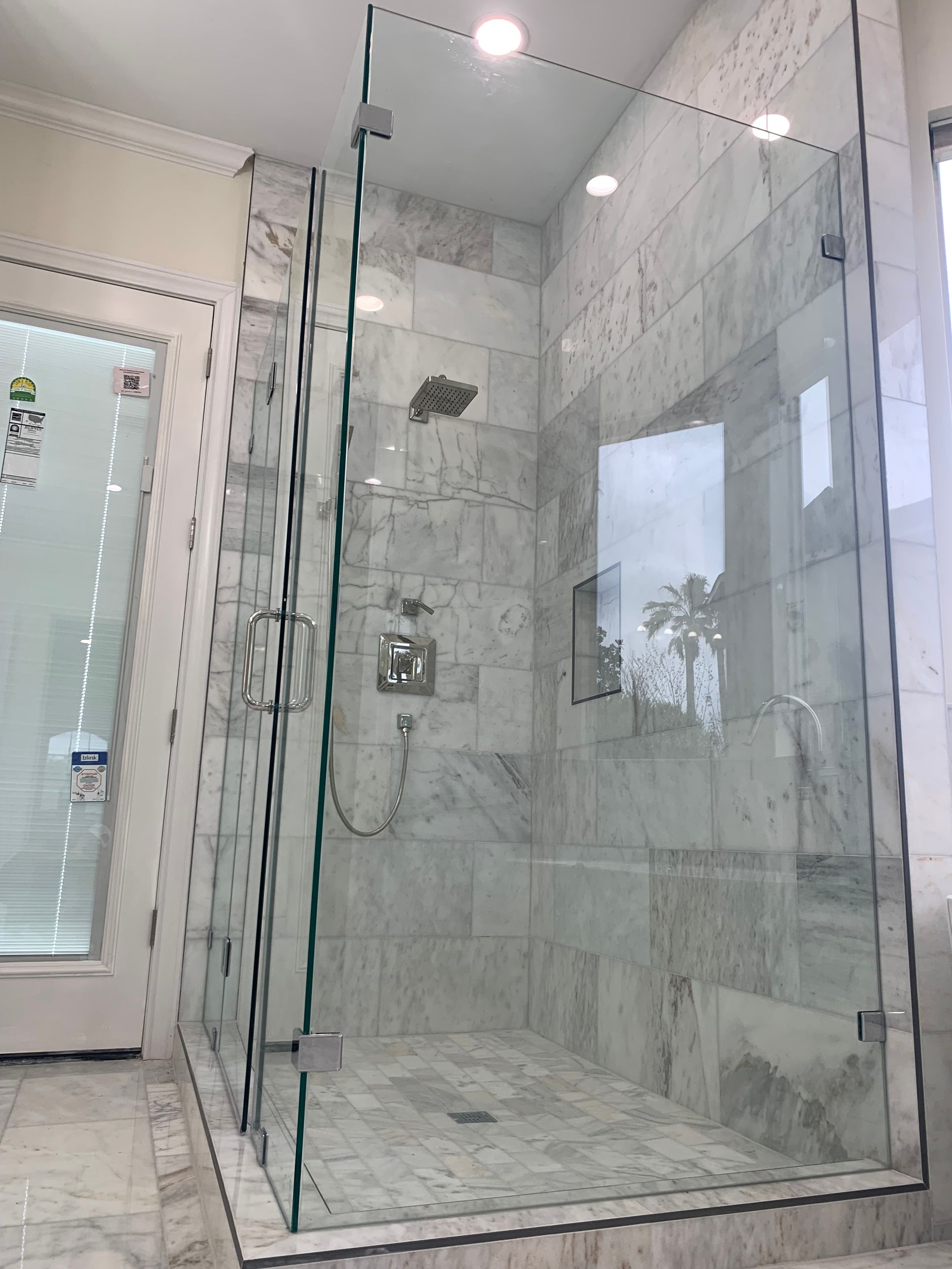 Glass-enclosed shower in a marble-tiled bathroom with a rainfall shower head and built-in niche.