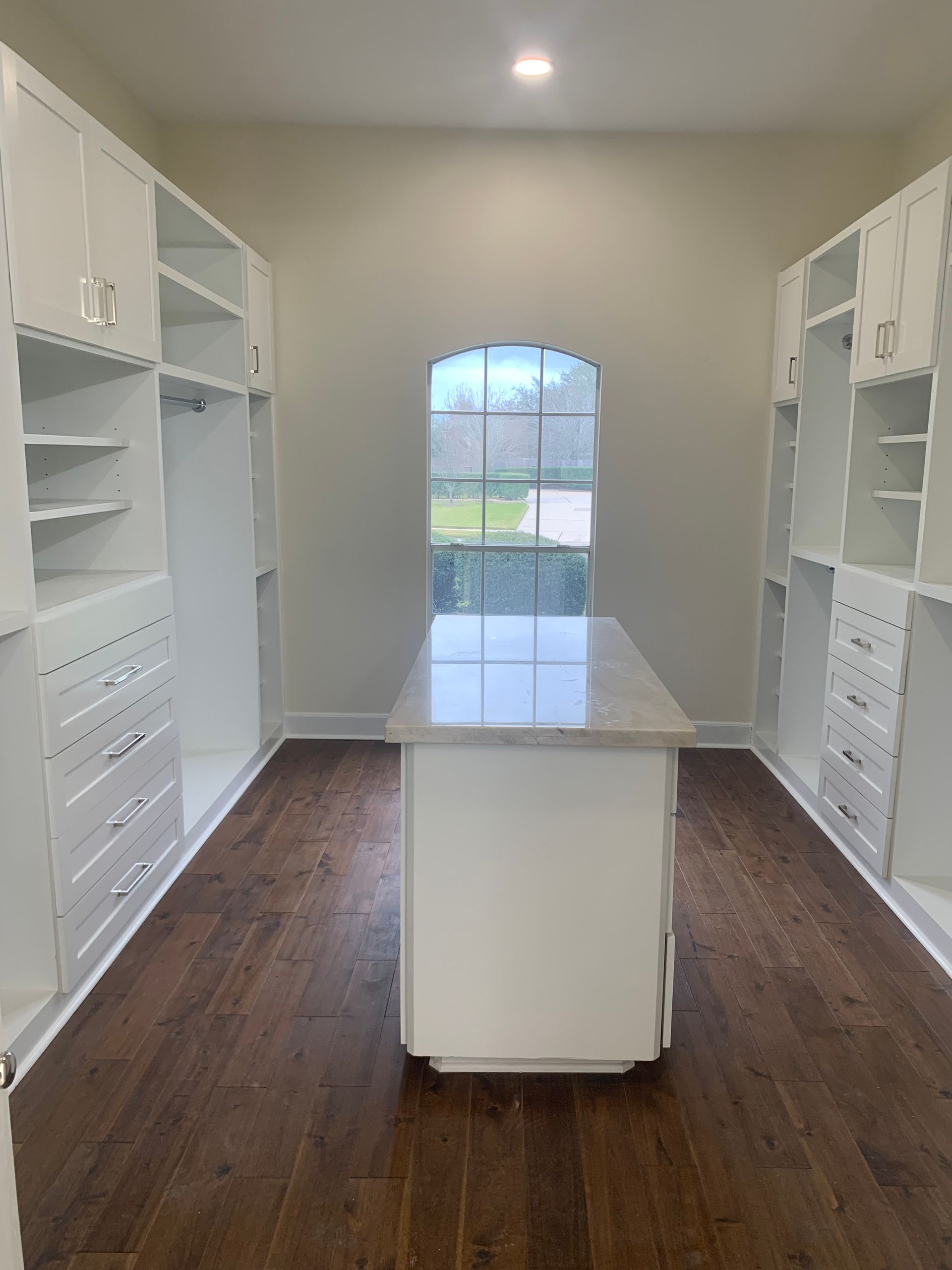 Walk-in closet with white cabinets, wood floors, and island. 