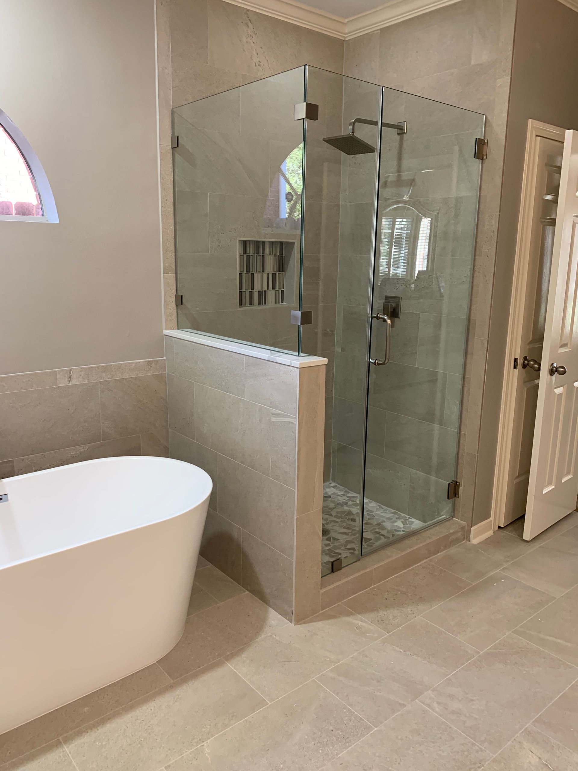 Modern bathroom with a glass-enclosed shower, freestanding tub, and light-colored tile.