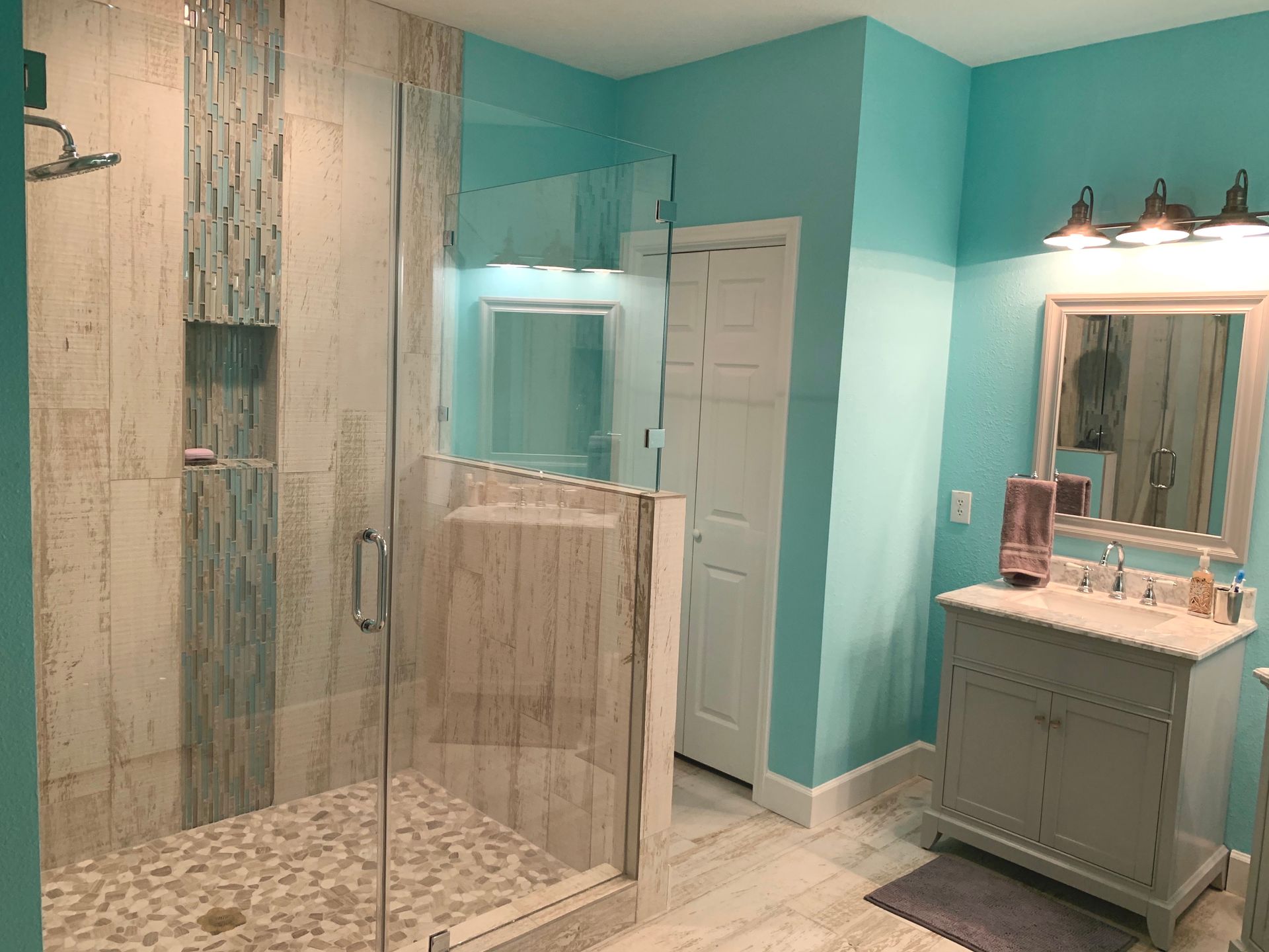 Bathroom with a blue-green color scheme. Shower, sink, mirror, and white door.