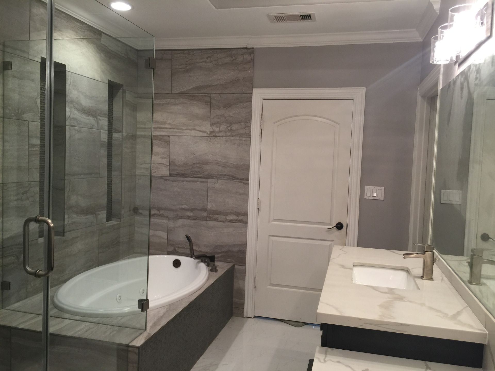 Bathroom with gray and white tile, a bathtub, a glass shower, and a white vanity.