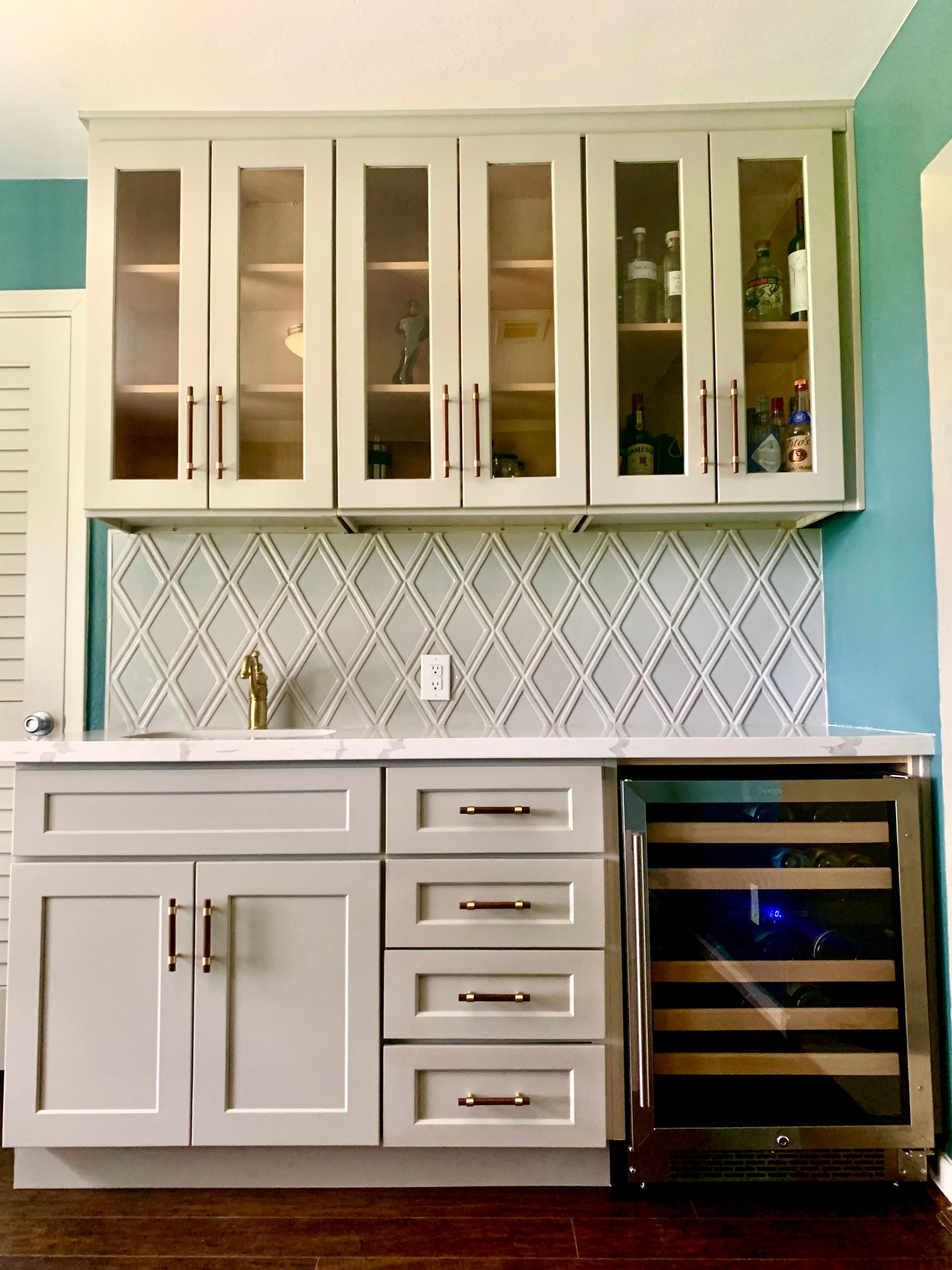 A built-in home bar with gray cabinets, marble countertop, and wine cooler.