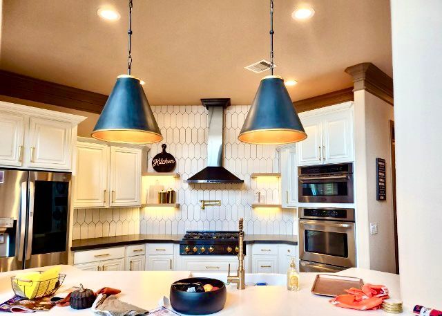Kitchen with white cabinets, dark blue pendant lights, and stainless steel appliances.