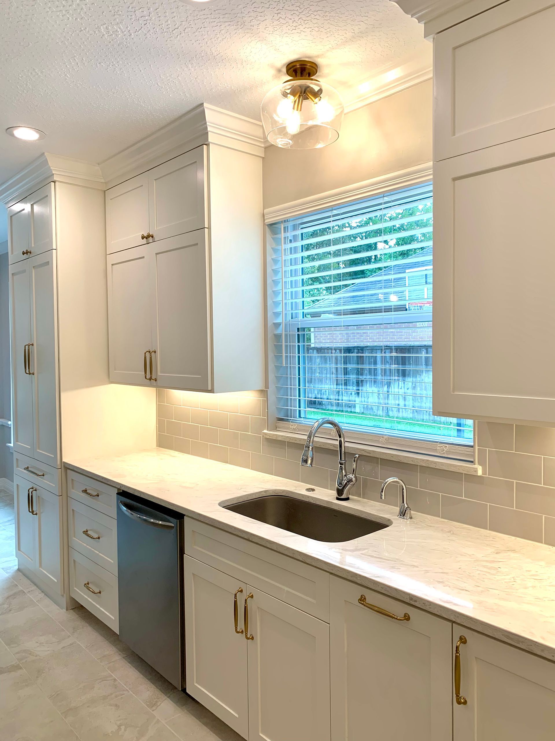 White kitchen with countertops, cabinets, sink, and a window with blinds.