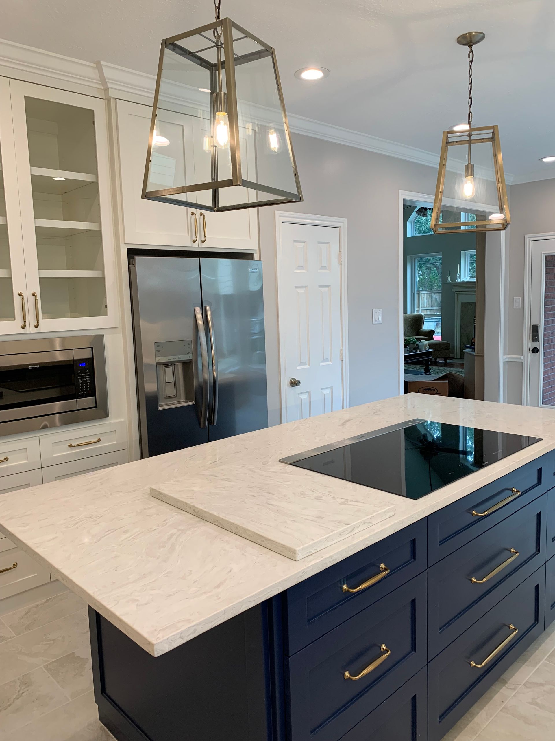 Blue kitchen island with cooktop and marble countertop, pendant lights, and stainless steel refrigerator.