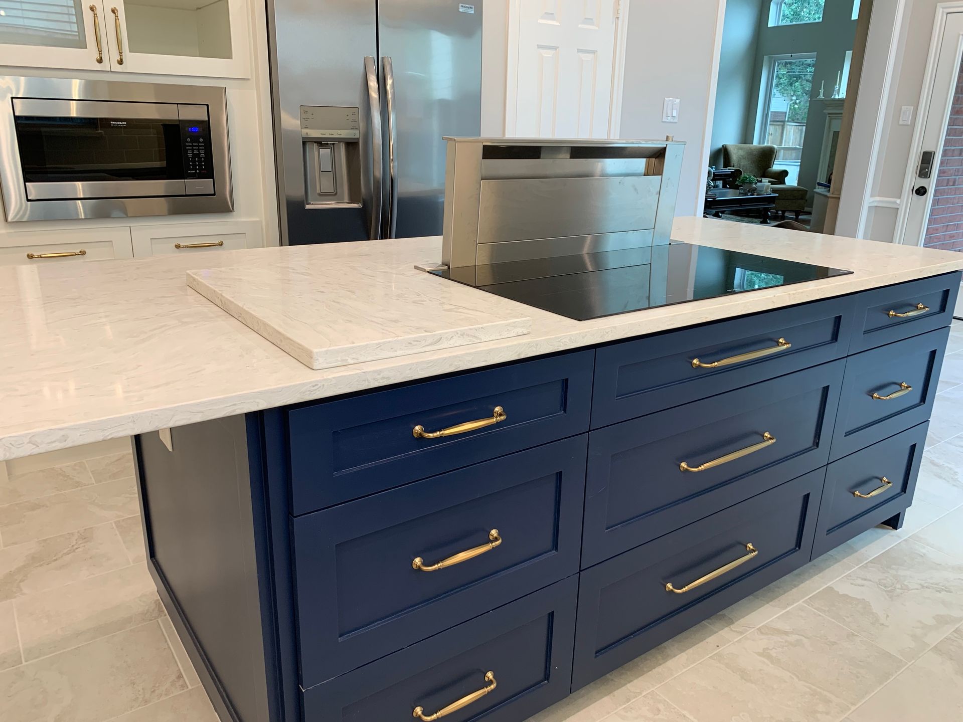 Blue kitchen island with a cooktop, drawers, and a white countertop. Stainless steel vent hood.