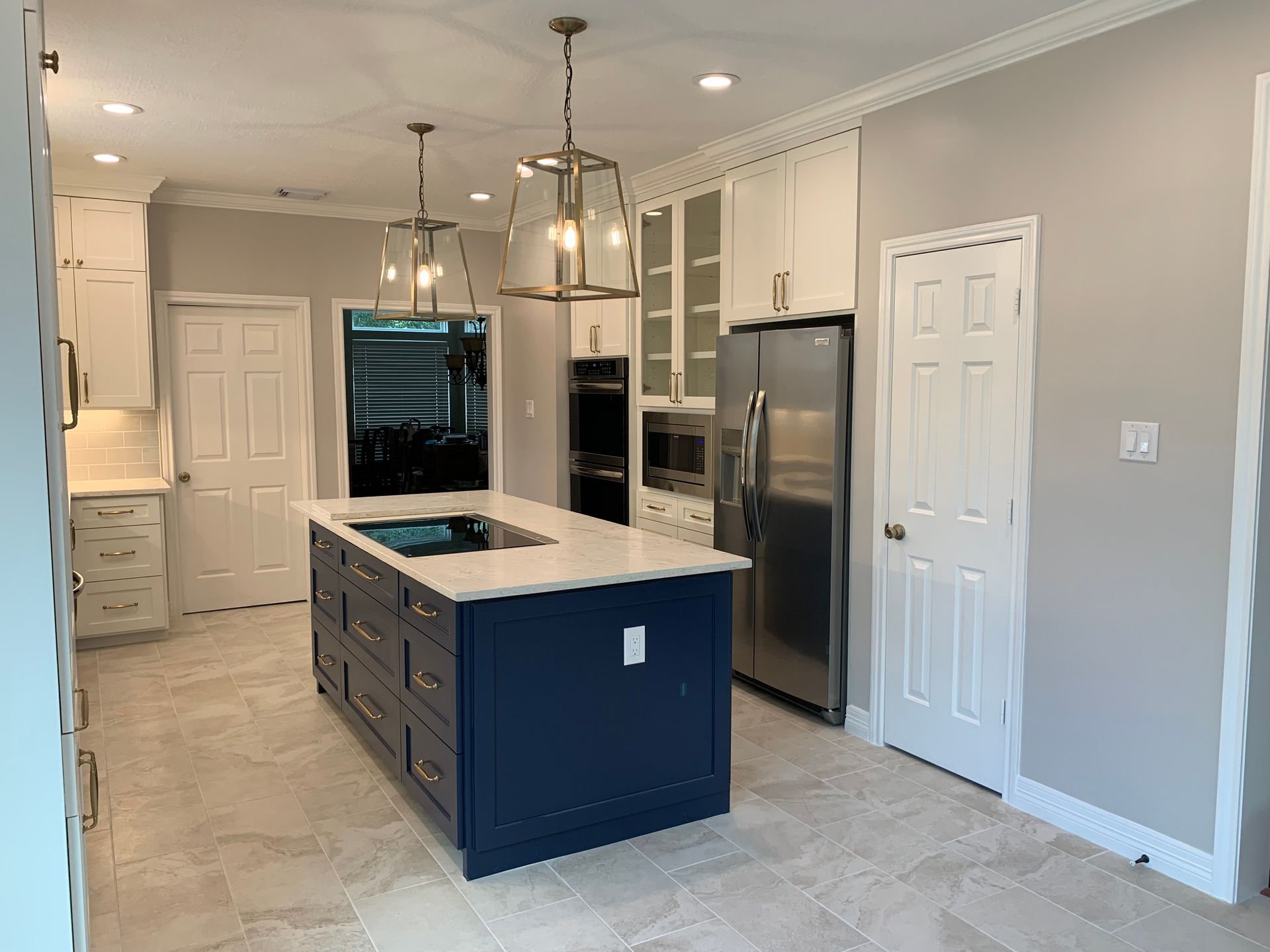 Kitchen with white cabinets, blue island, stainless steel appliances, and beige tile floor.