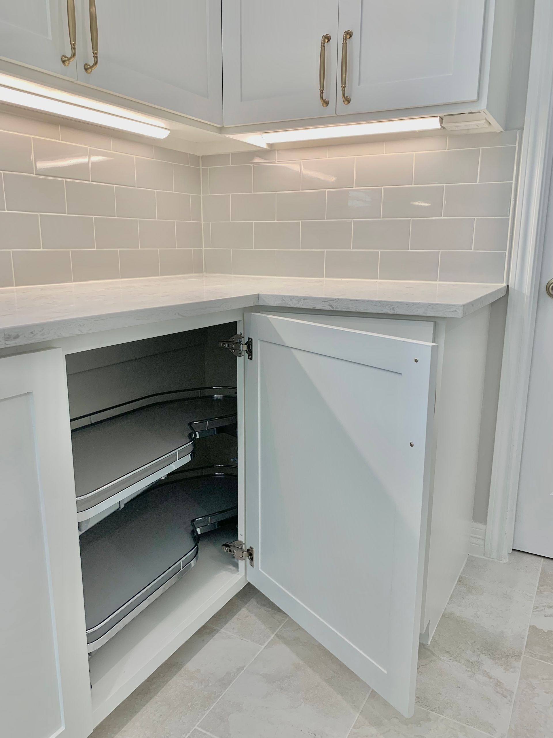 White kitchen cabinet with open door revealing pull-out shelves, countertop, and tiled backsplash.