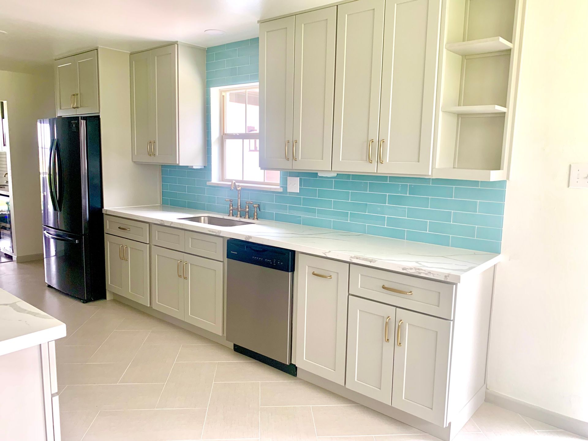 Modern kitchen with light gray cabinets, blue tile backsplash, stainless steel appliances, and white countertops.