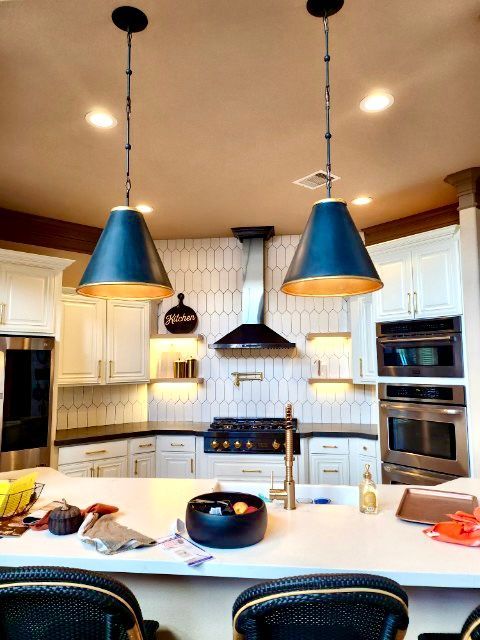Kitchen with white cabinets, dark blue pendant lights, and stainless steel appliances.