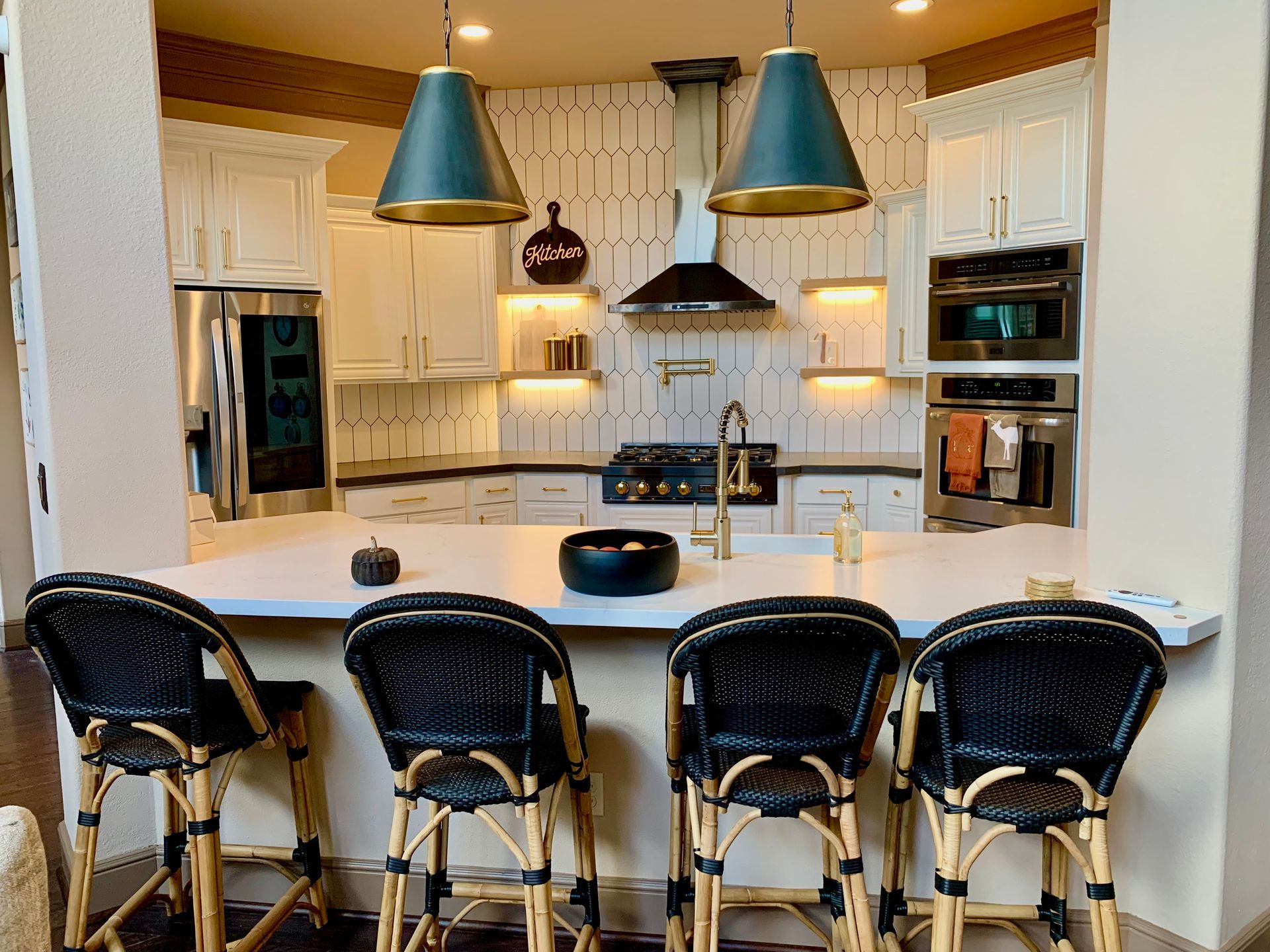Kitchen with white cabinets, island with black woven bar stools, and teal pendant lights.