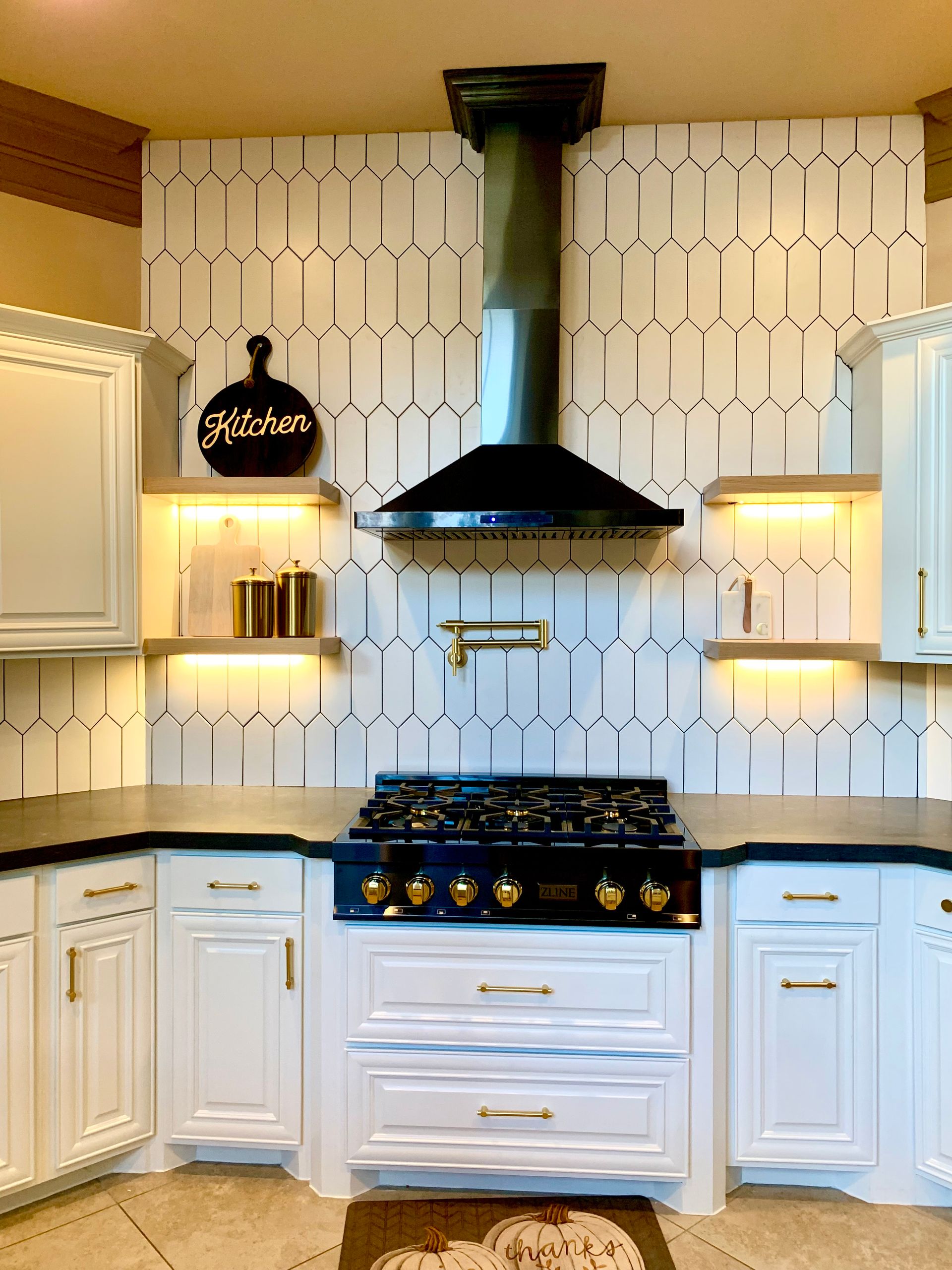 White kitchen with black stovetop, range hood, and geometric tile backsplash.