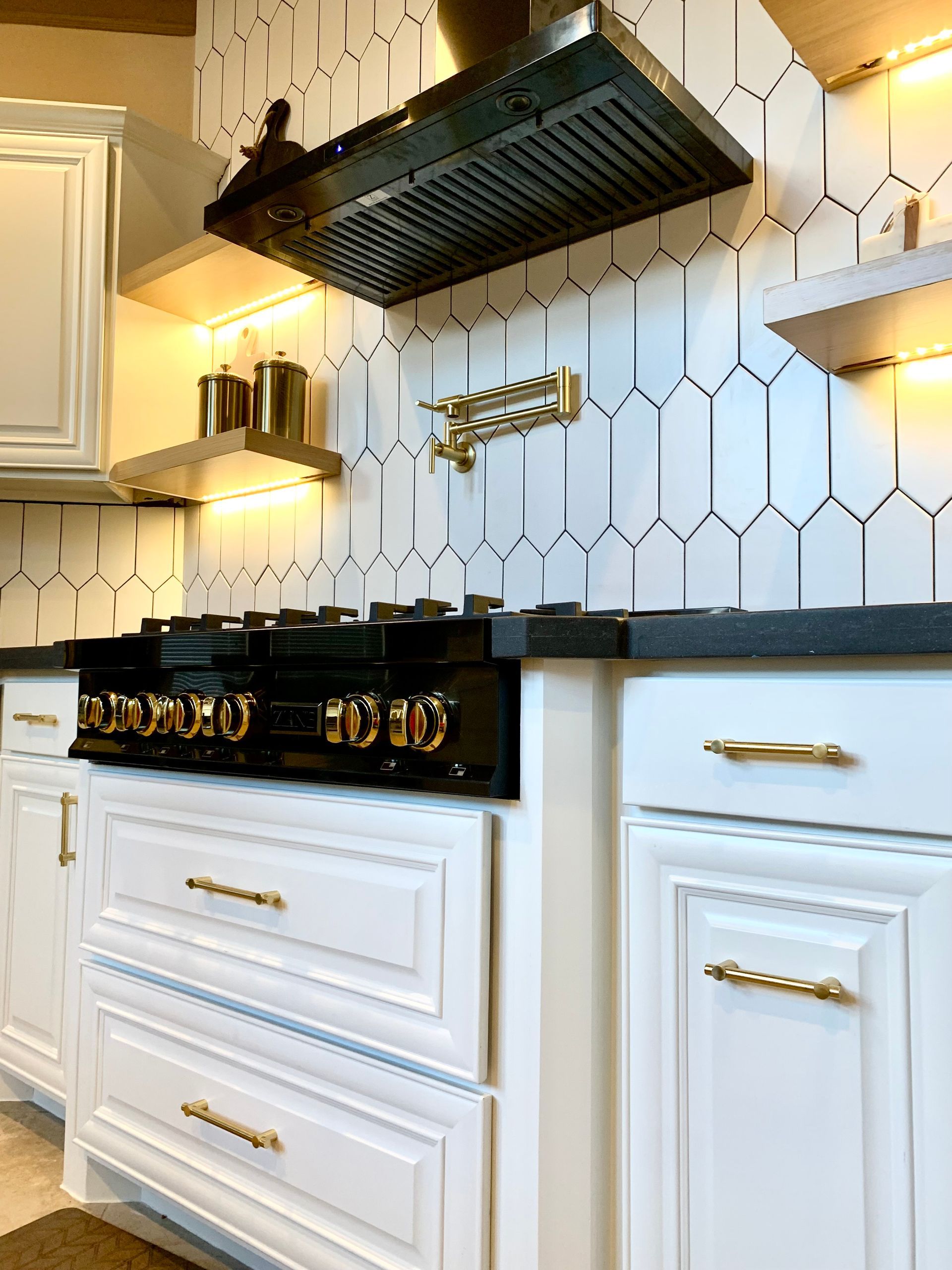 White kitchen with black stove and range hood, gold accents, and geometric backsplash.