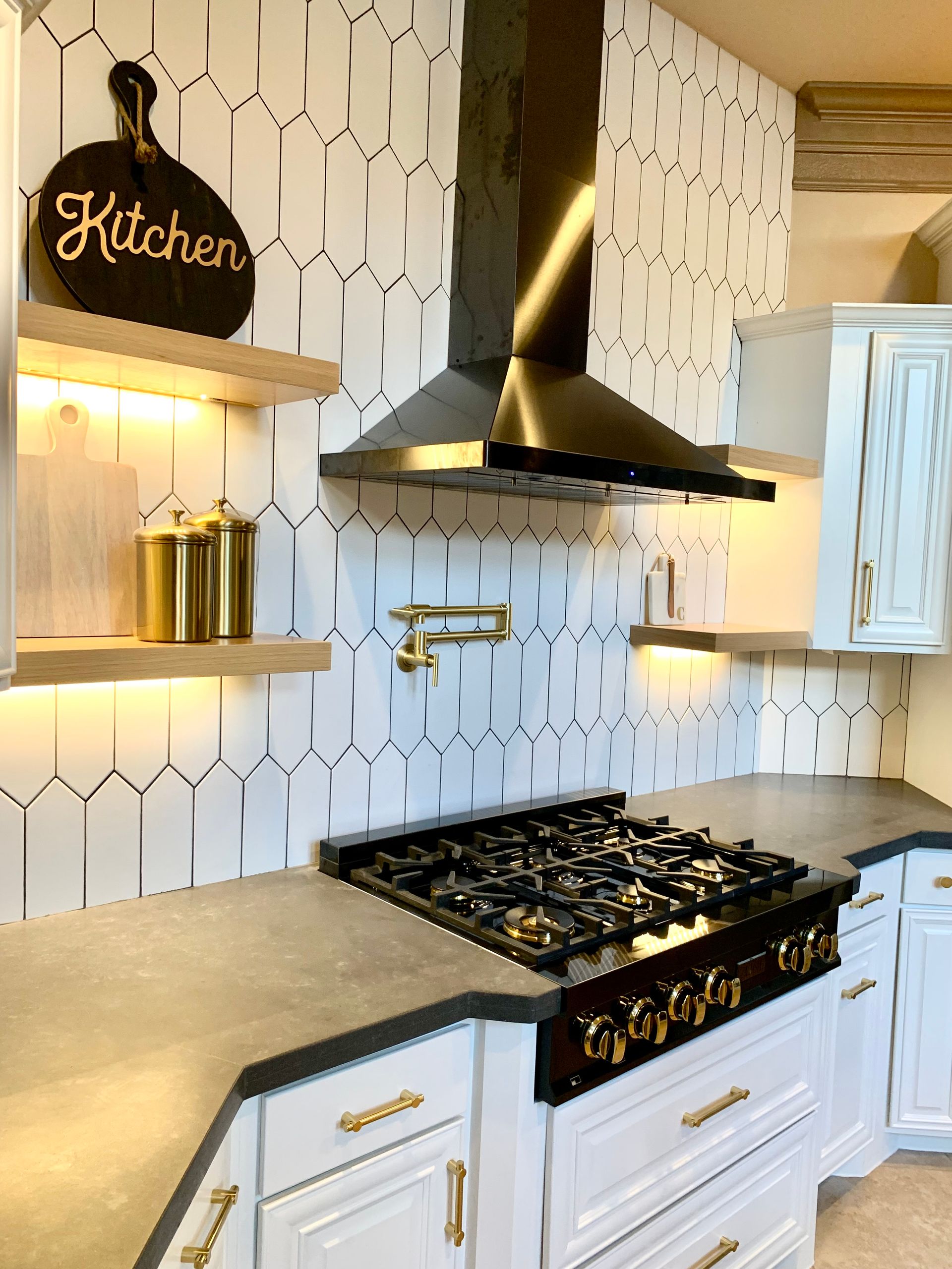 Modern kitchen with white cabinets, dark stovetop, patterned tile backsplash, and floating shelves.