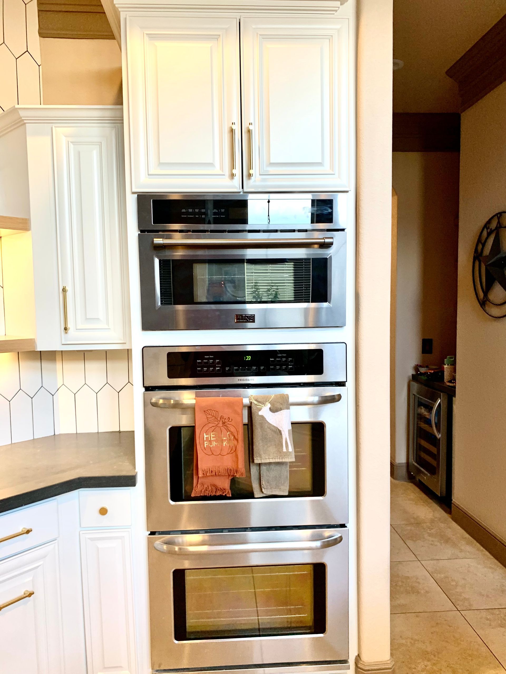 Built-in stainless steel oven and microwave tower in a white kitchen with upper cabinets.
