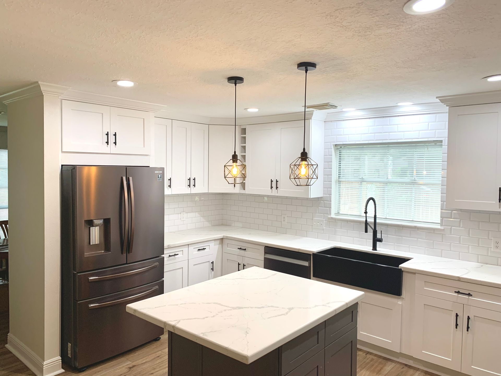 Modern white kitchen with stainless steel appliances, dark island, and pendant lights.